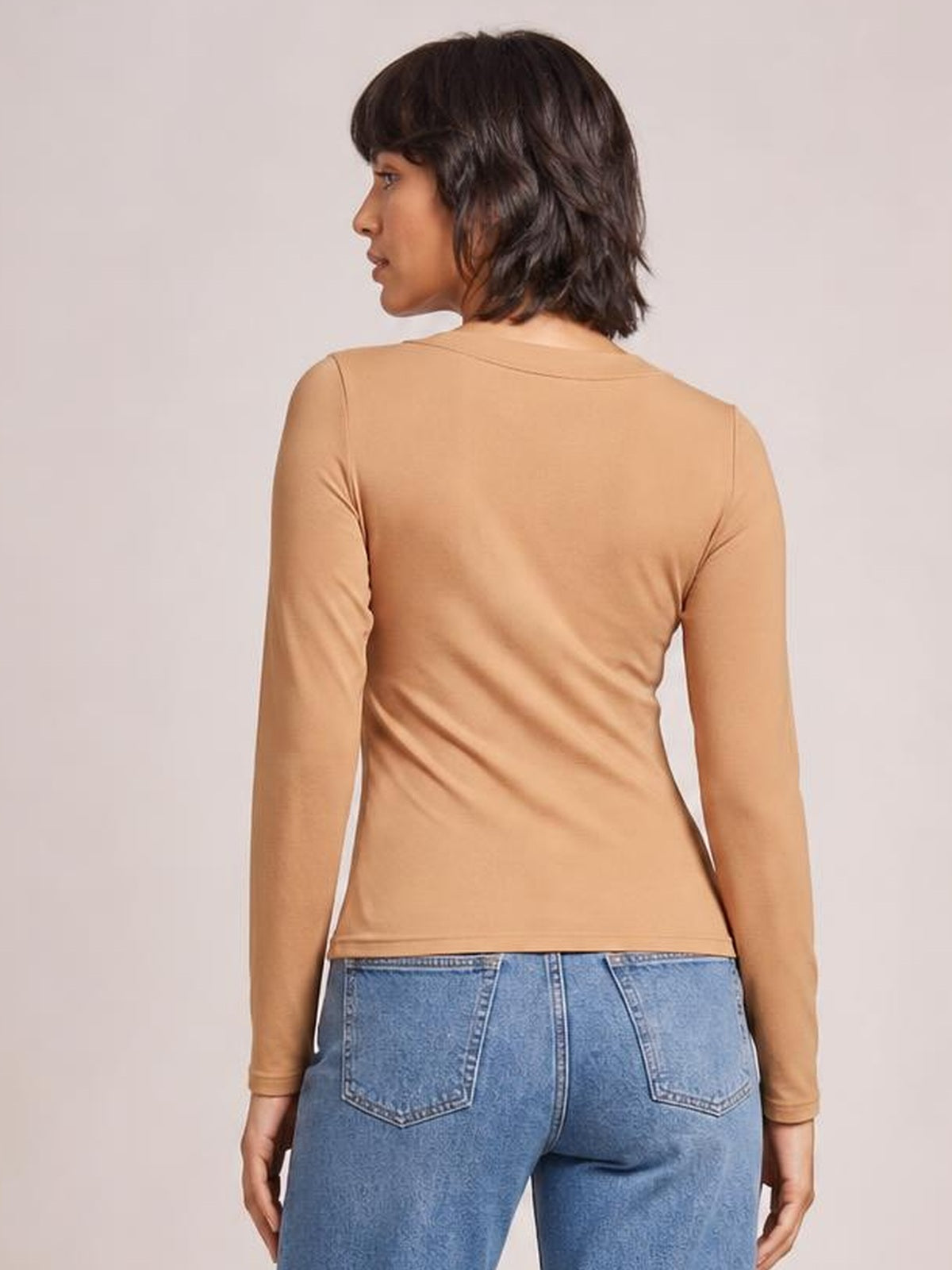 Model shown from behind wearing a tan round neck long sleeve T-shirt with a fitted silhouette, smooth construction, and straight hem.