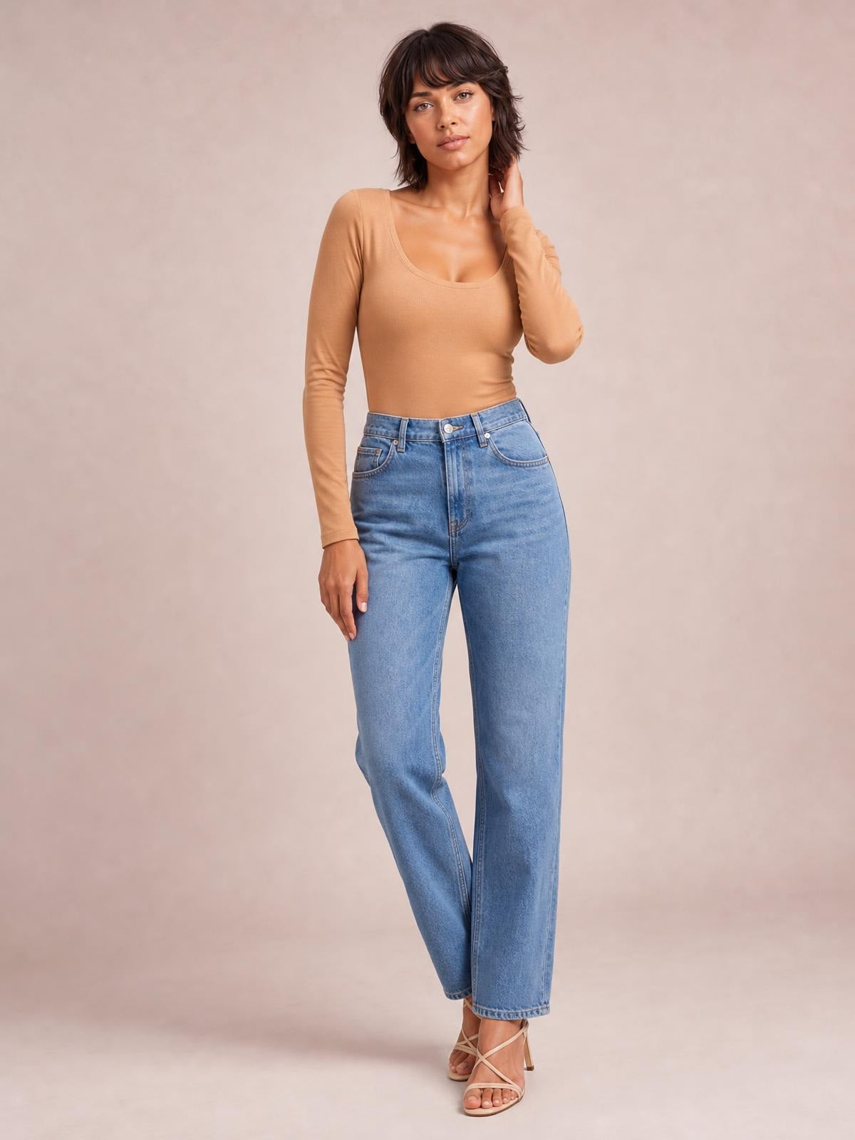 A model poses in a fitted tan round neck long sleeve T-shirt with subtle ribbed texture, a smooth silhouette, and slightly stretchy construction.