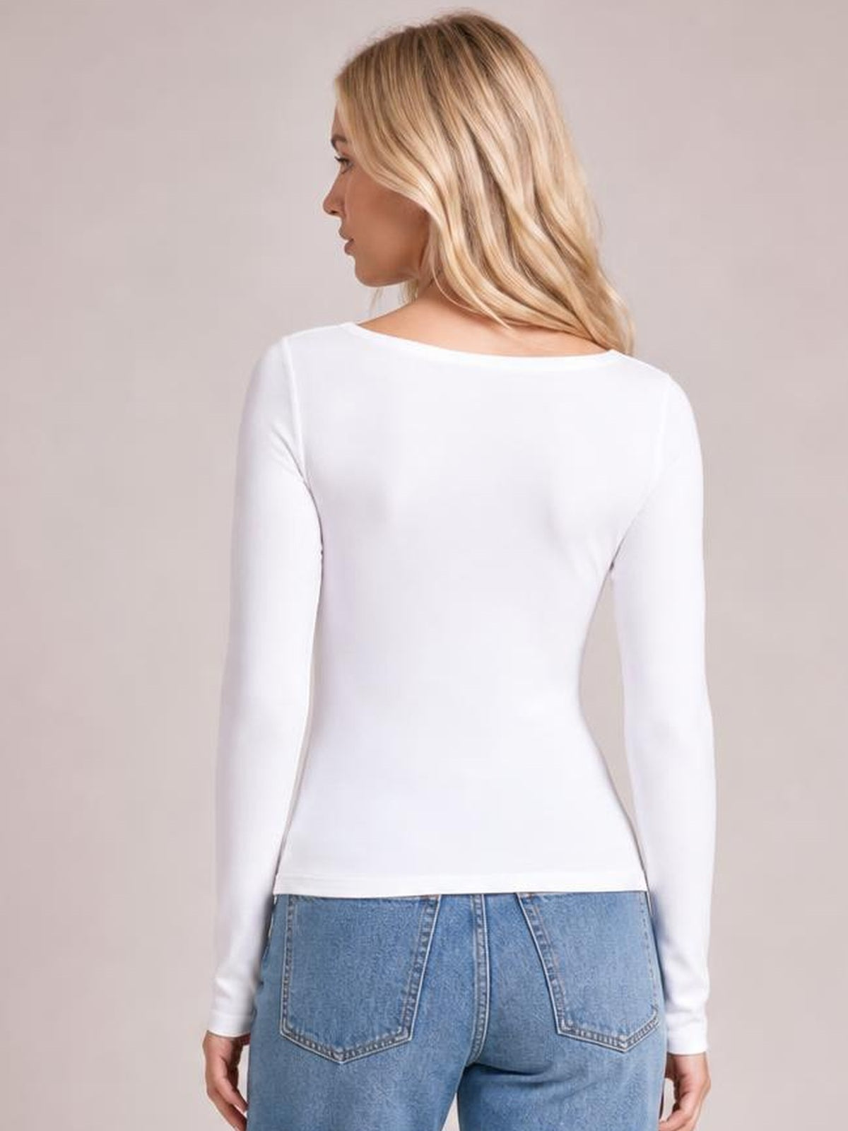 Model turned slightly away wears a white round-neck long-sleeve T-shirt with a smooth, fitted silhouette and simple construction.