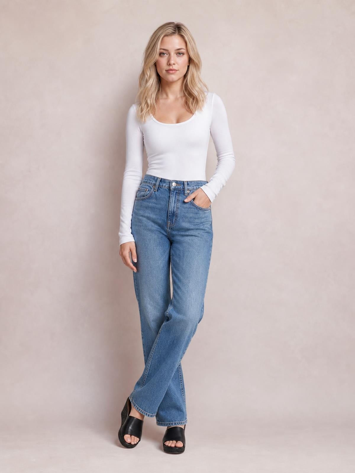 A model poses in a white round-neck long-sleeve T-shirt with a fitted silhouette and smooth construction, one hand resting in her jeans pocket.