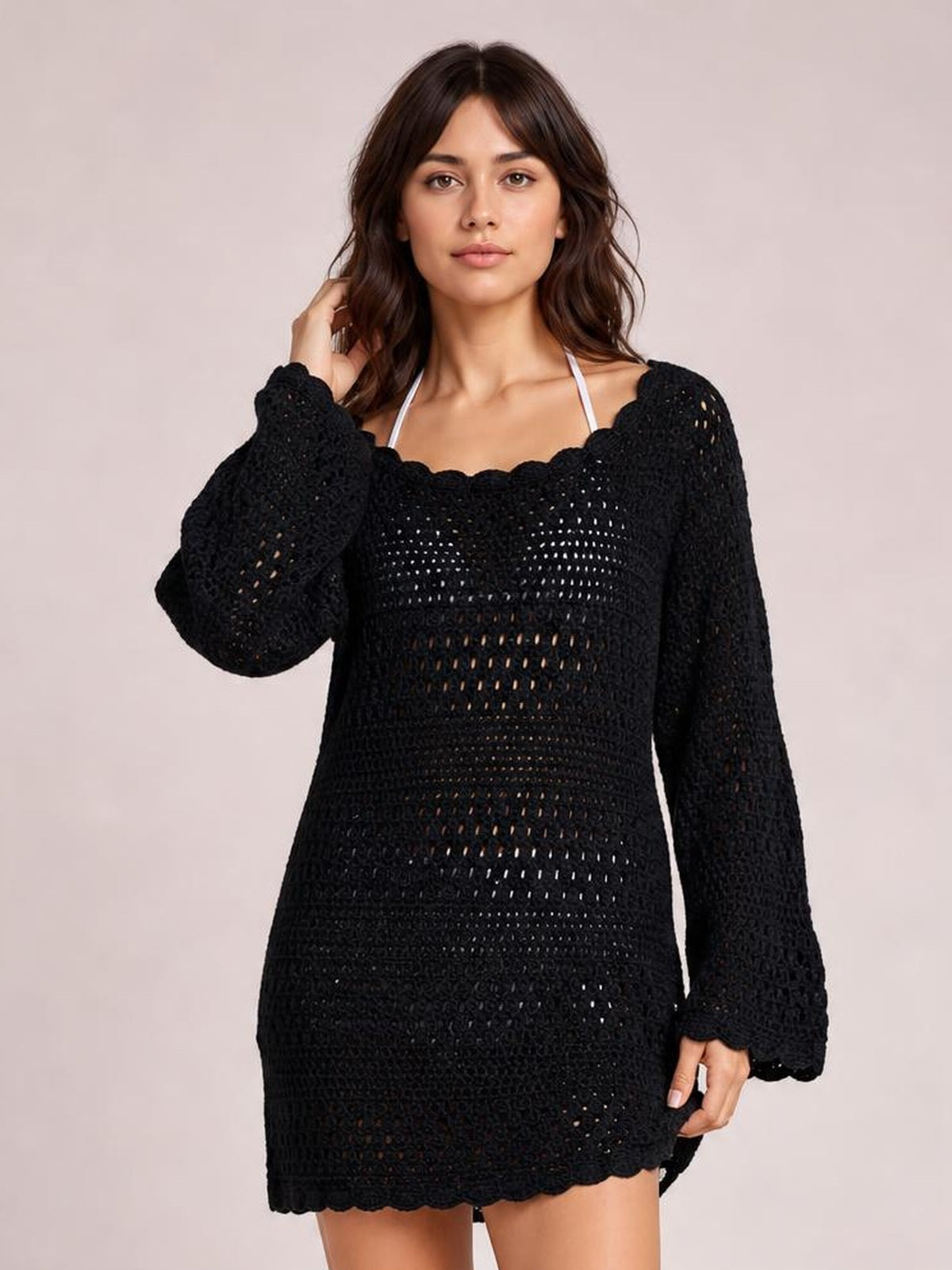 Model wearing a black round neck openwork cover-up with a relaxed tunic silhouette, long sleeves, cutout knit construction, and scalloped trim.