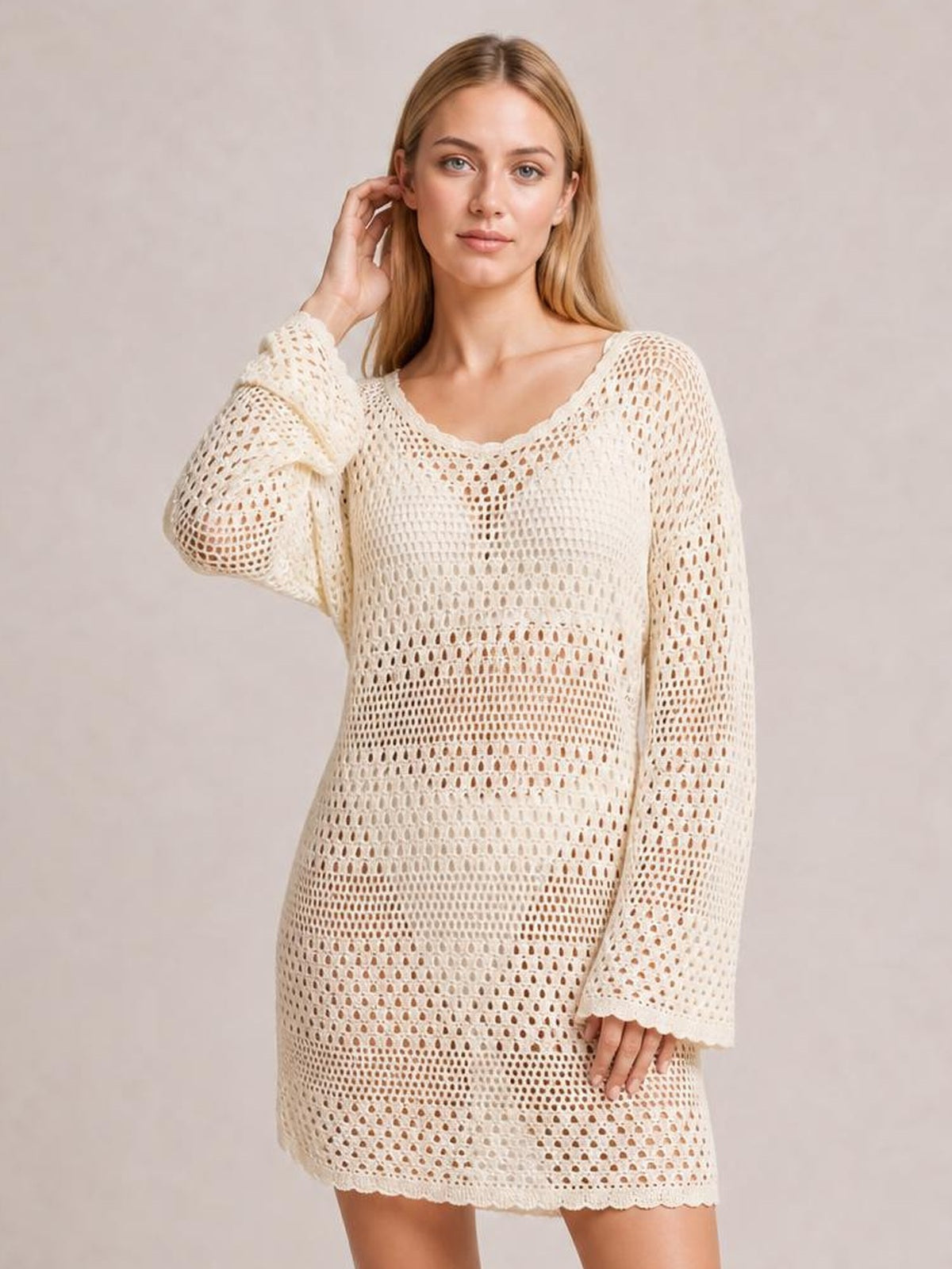Model wears an ivory round neck openwork cover-up with long sleeves, a loose tunic silhouette, cutout knit construction, and scalloped hem.