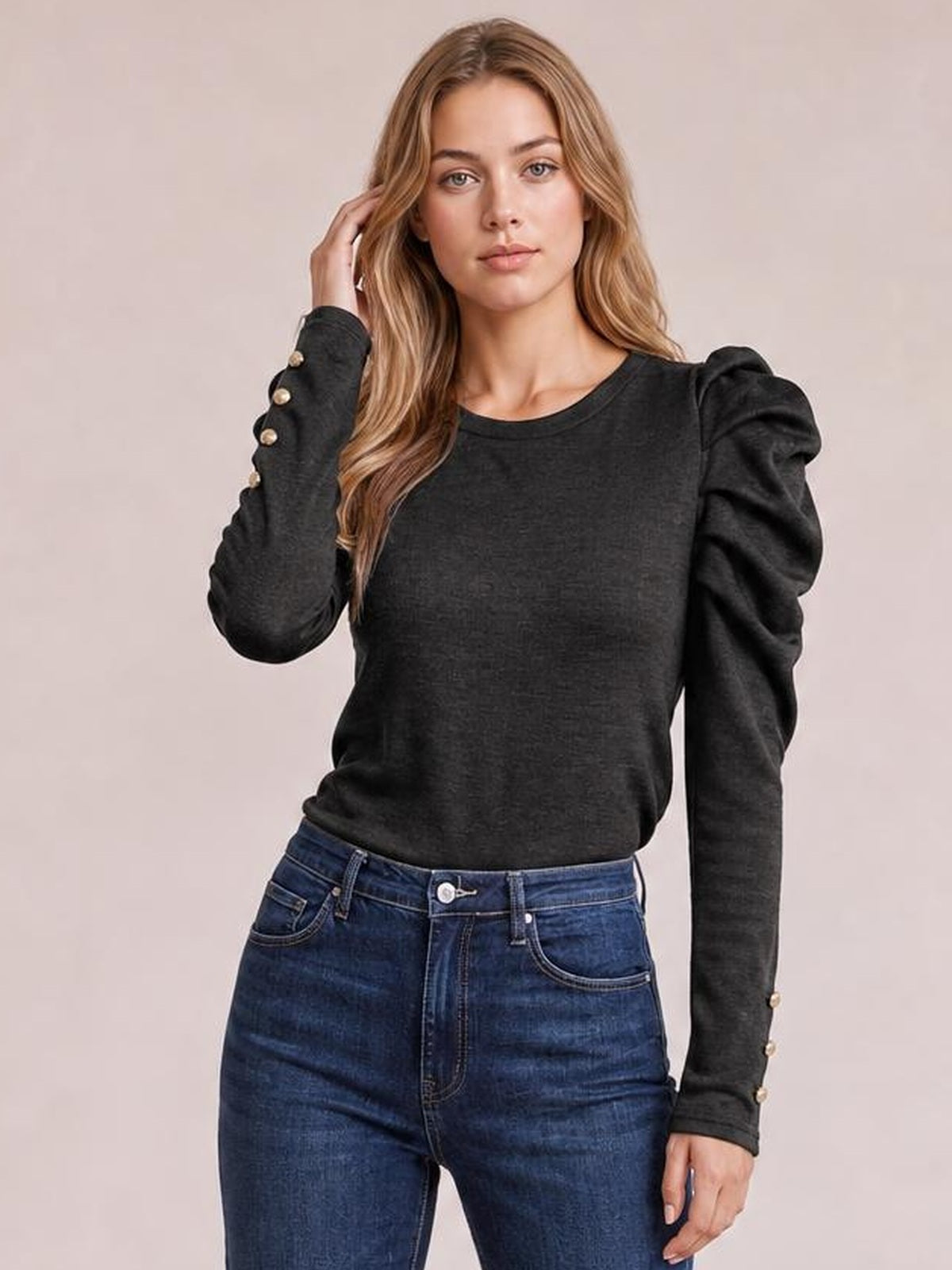 Model poses in a black round-neck blouse with voluminous puff sleeves, a fitted silhouette, and decorative gold buttons along the cuffs.