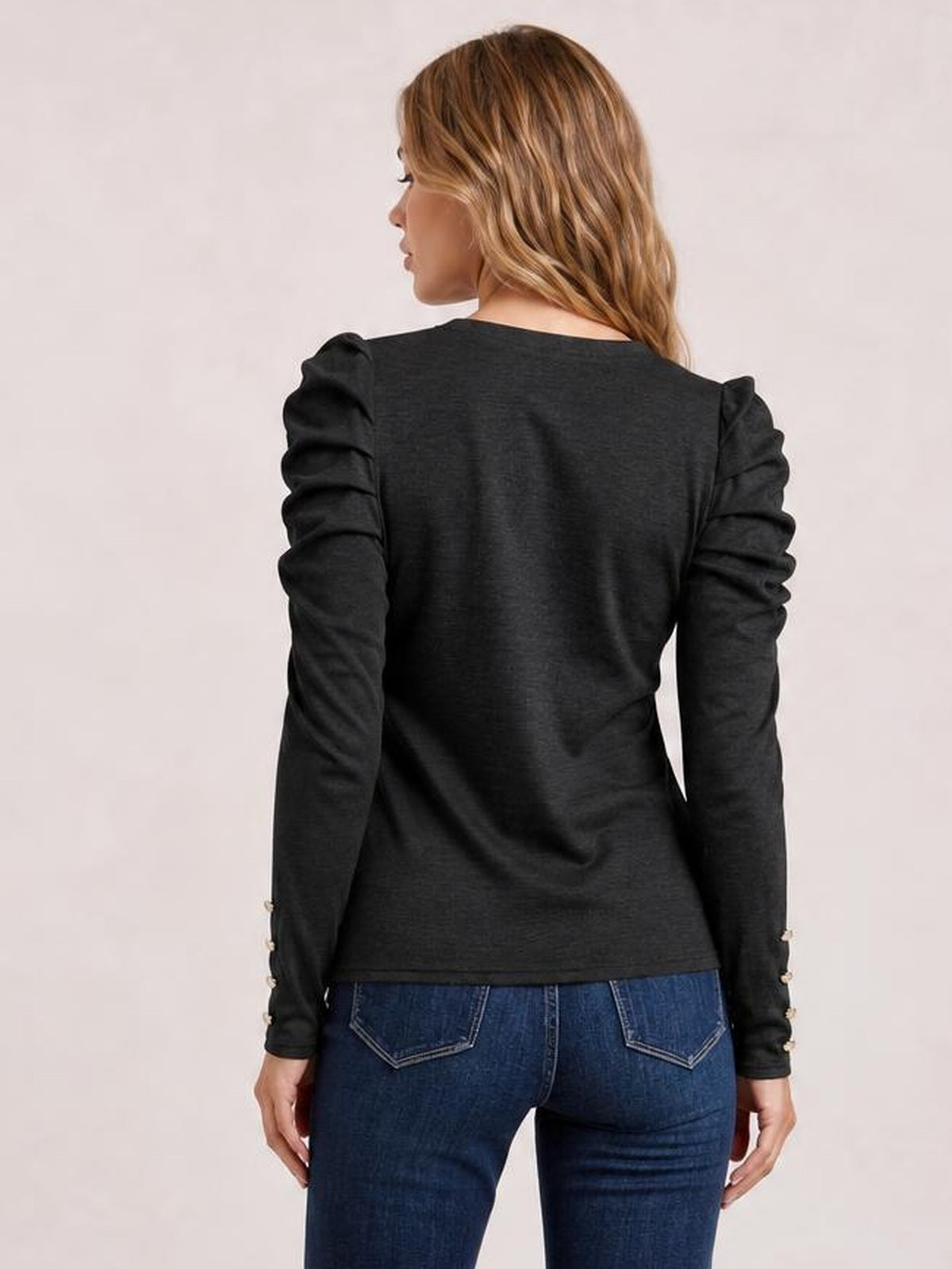 A model wears a black round-neck blouse with gathered puff sleeves and a slim silhouette, shown from the back with her arms relaxed.