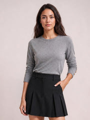 Model wearing a gray round-neck blouse with long slightly ruched sleeves and a relaxed straight silhouette, posed with one hand in a pocket.