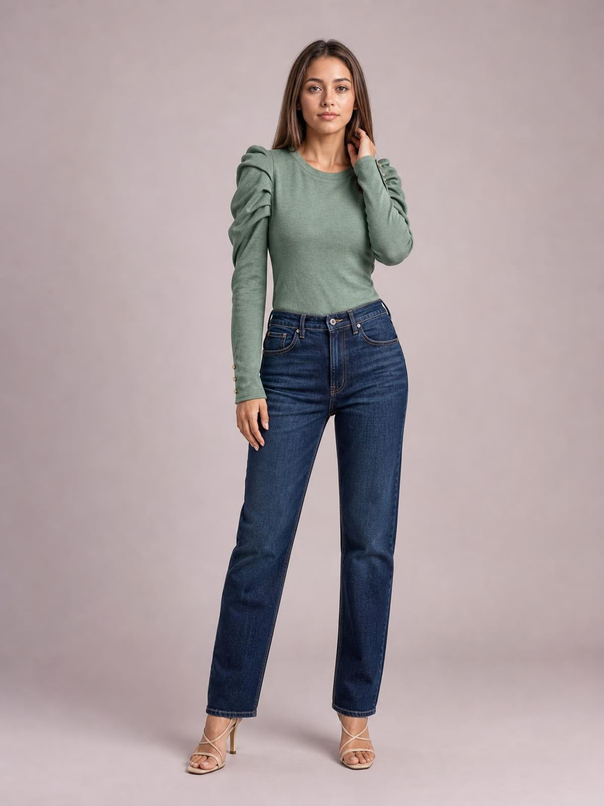 Model stands in a sage green round neck blouse with voluminous ruched puff sleeves, fitted silhouette, and buttoned cuffs, touching her hair.