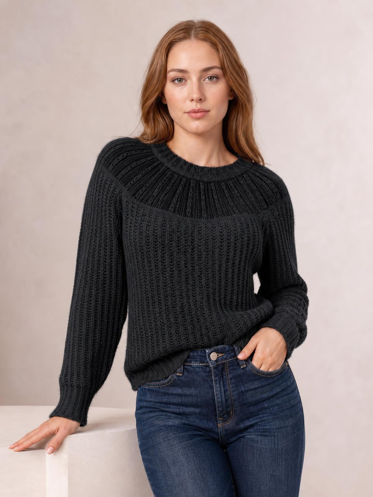 Model wearing a black round-neck rib-knit sweater with a textured yoke, long sleeves, and a relaxed silhouette, one hand in her jeans pocket.