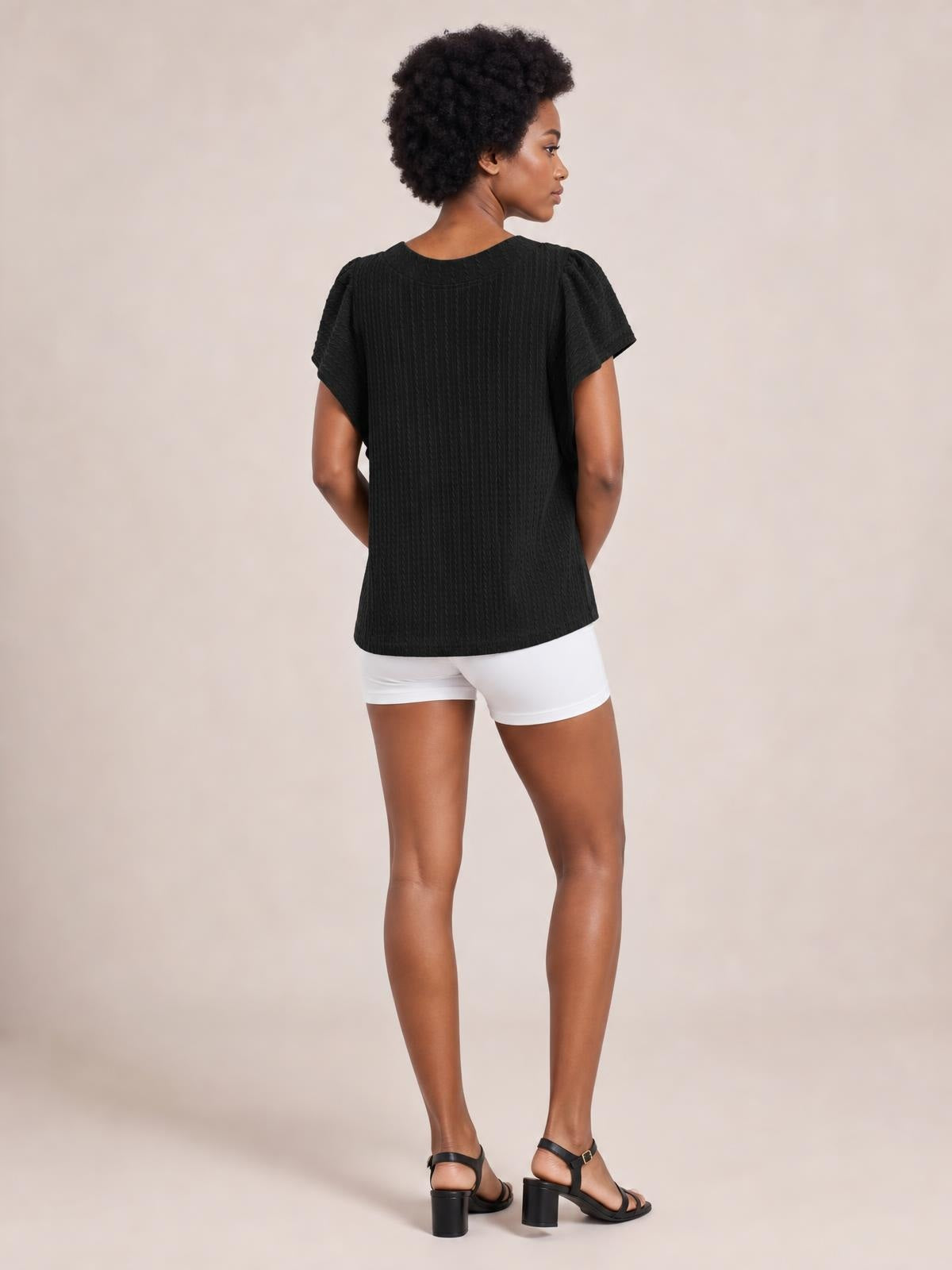 A model poses turned away in a black round neck ruffle sleeve top with a relaxed straight silhouette and subtly textured construction.