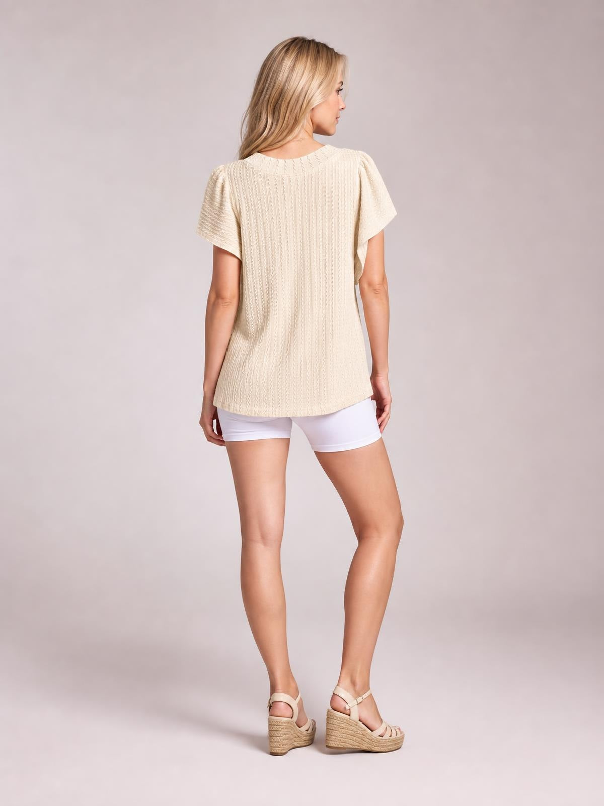 Model turned away wears a cream round-neck top with short sleeves, textured vertical construction, a relaxed straight silhouette, and curved hem.