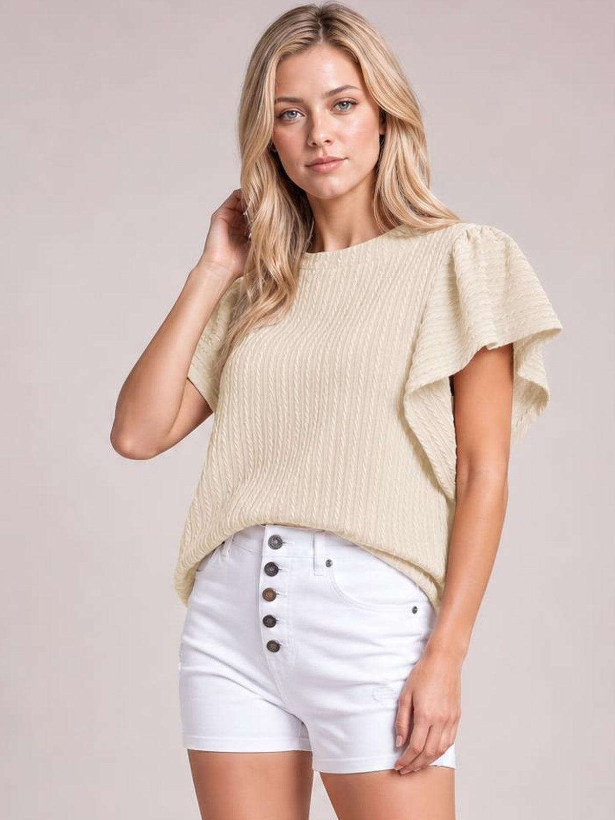 A model poses in a cream round-neck top with textured fabric, layered ruffle short sleeves, and a relaxed, slightly loose silhouette.