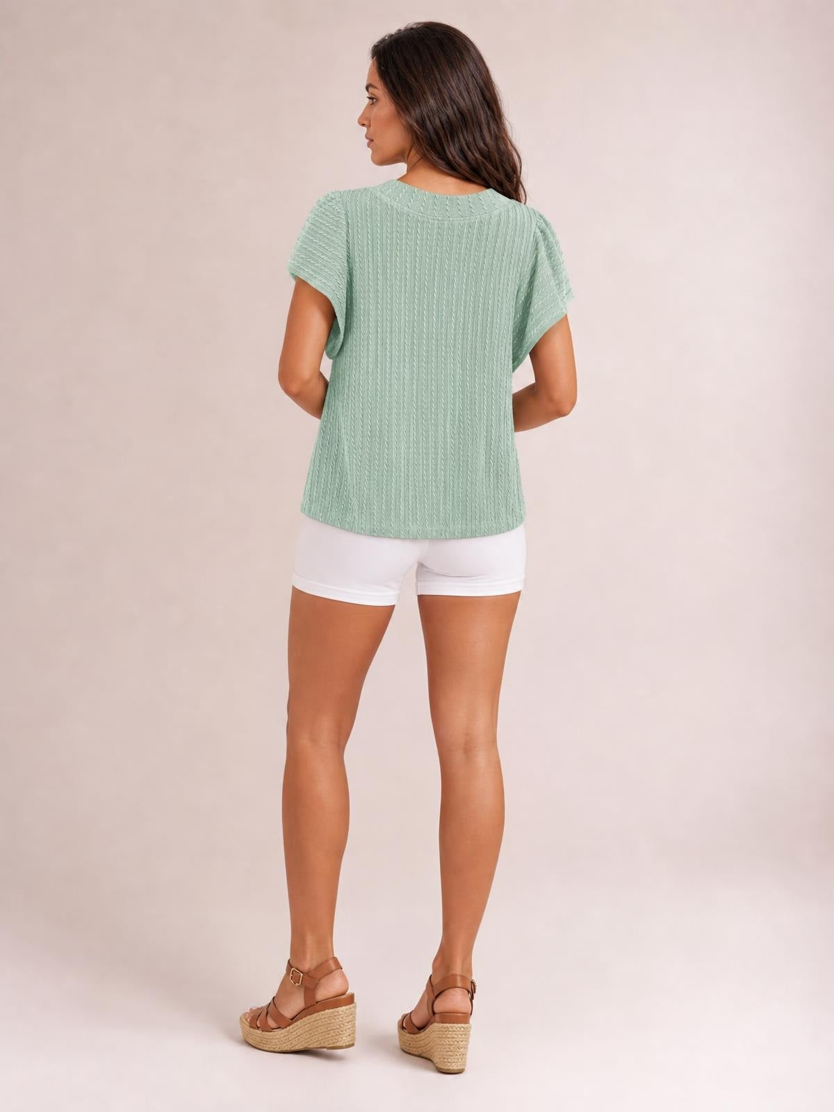 Model shown from behind in a sage green round neck ruffle sleeve top with a textured finish, relaxed straight silhouette, and hands resting at her waist.