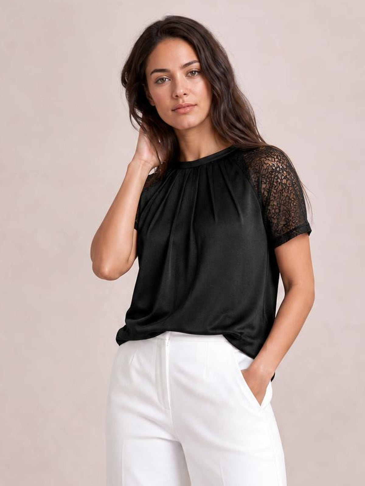 Model poses in a black round neck short sleeve T-shirt with lace sleeves, pleated front detailing, and a relaxed draped silhouette.