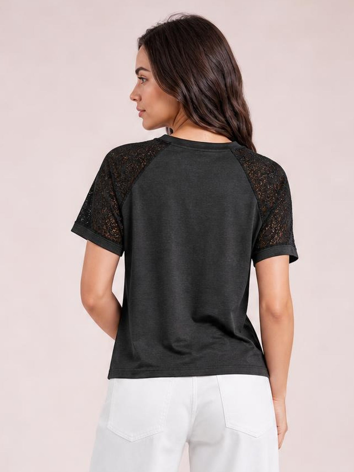 Model turned slightly away to show a black round neck short sleeve T-shirt with lace raglan sleeves, cuffed hems, and a relaxed silhouette.