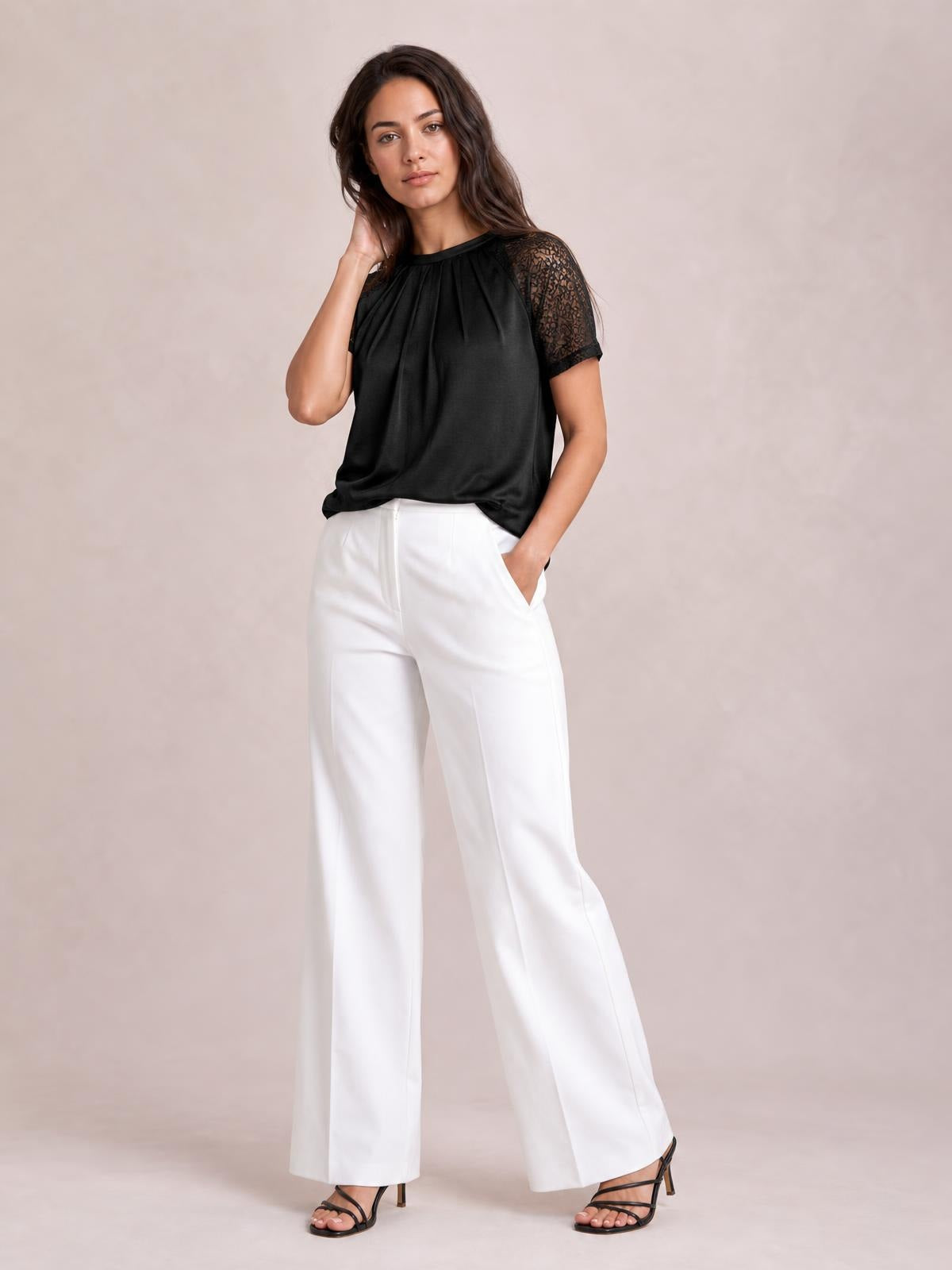 Model wears a black round neck short sleeve T-shirt with lace sleeves and a softly draped silhouette, posing with one hand in her pocket.