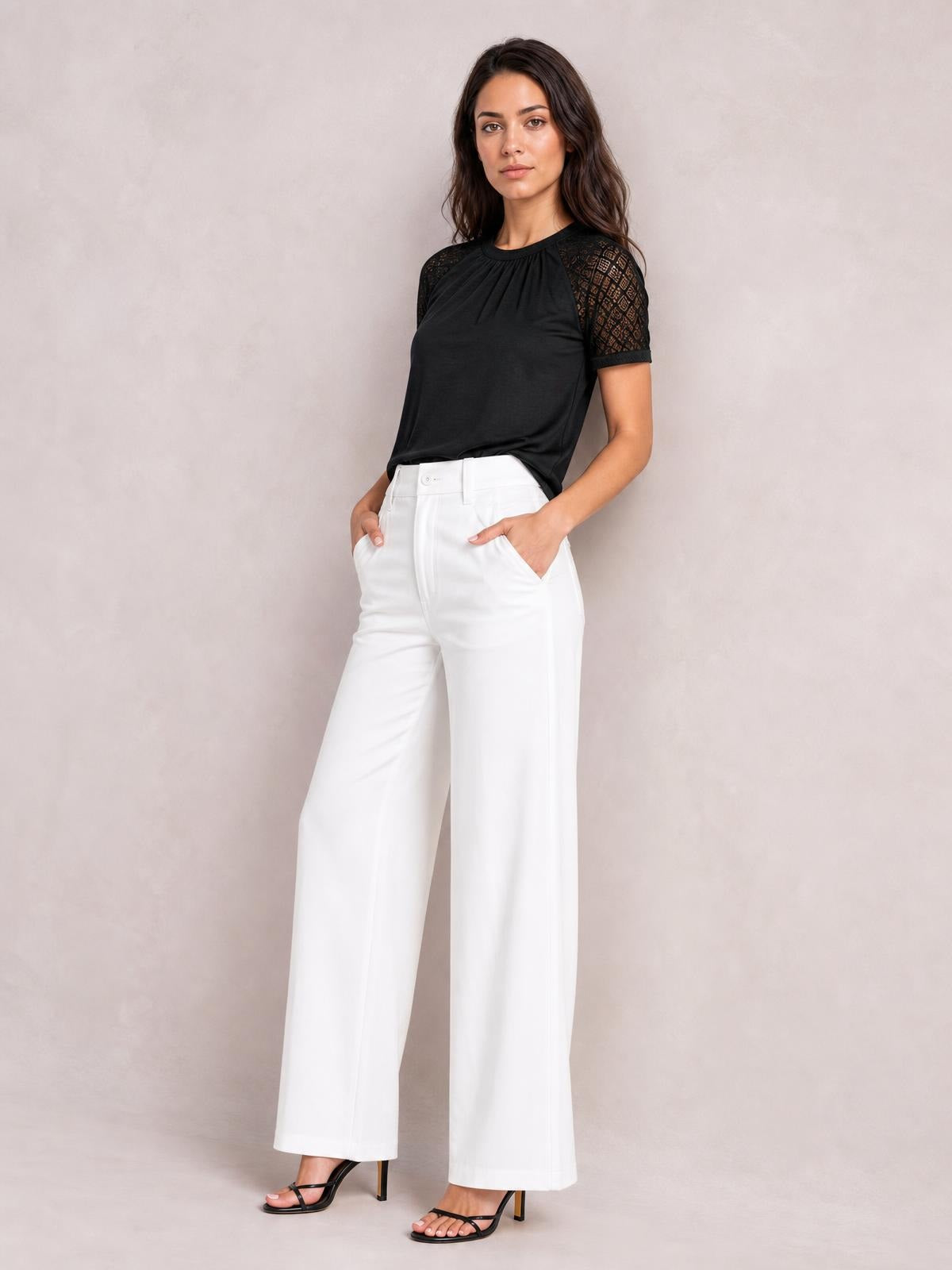A model poses with hands in her pockets wearing a black round neck short sleeve T-shirt with gathered detailing and patterned lace sleeves.