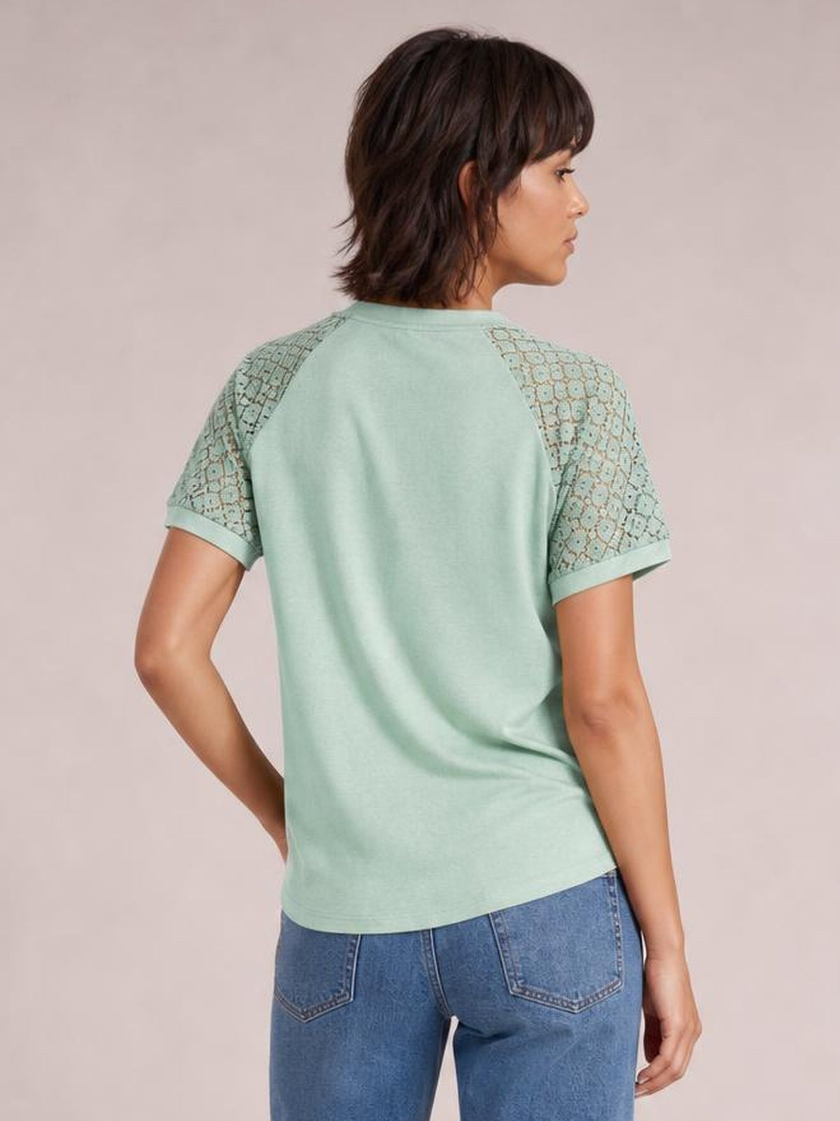 Model shown from the back in a mint green round neck short sleeve T-shirt with lace-paneled sleeves, rolled cuffs, and a relaxed straight silhouette.