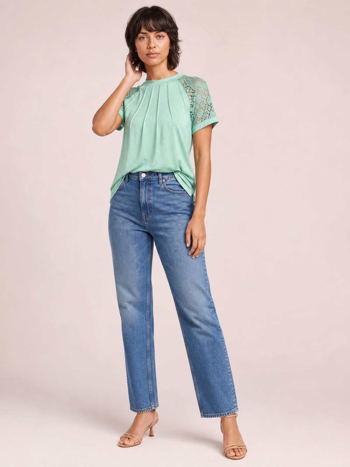 Model wearing a mint green round neck short sleeve T-shirt with lace shoulder details and a relaxed silhouette, posing with one hand touching her hair.
