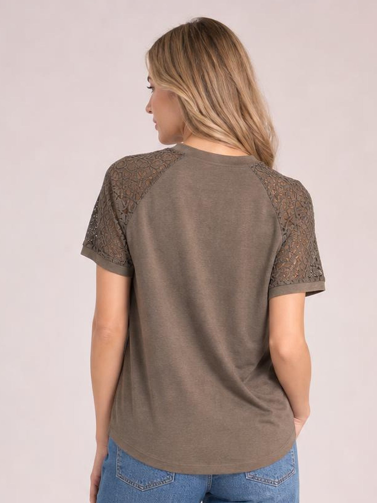 A model stands facing away in a taupe round-neck short-sleeve T-shirt with lace shoulder panels, lace sleeves, and a relaxed straight silhouette.