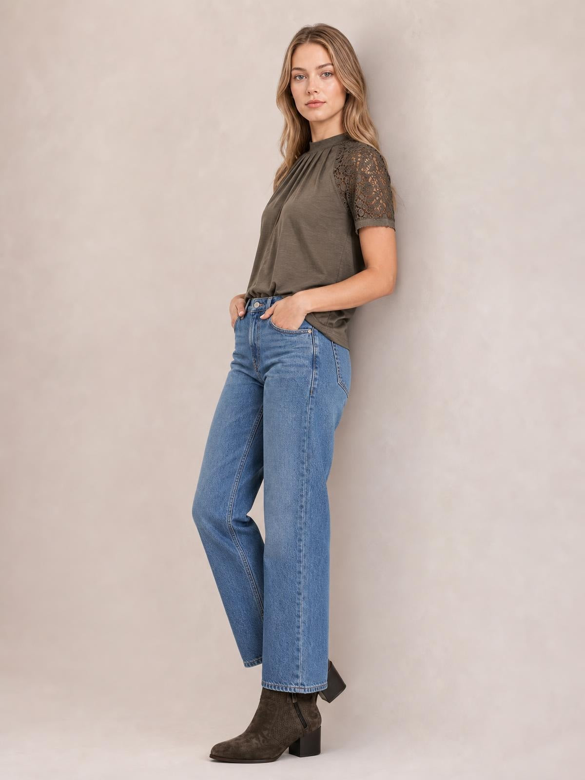 Model poses with hands in her pockets wearing a taupe round neck short sleeve T-shirt with lace-detail sleeves and a relaxed silhouette.