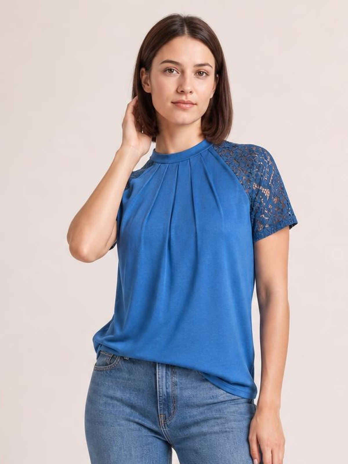 Model wearing a royal blue round neck short sleeve T-shirt with pleated front, lace sleeve details, and a relaxed silhouette while touching her hair.