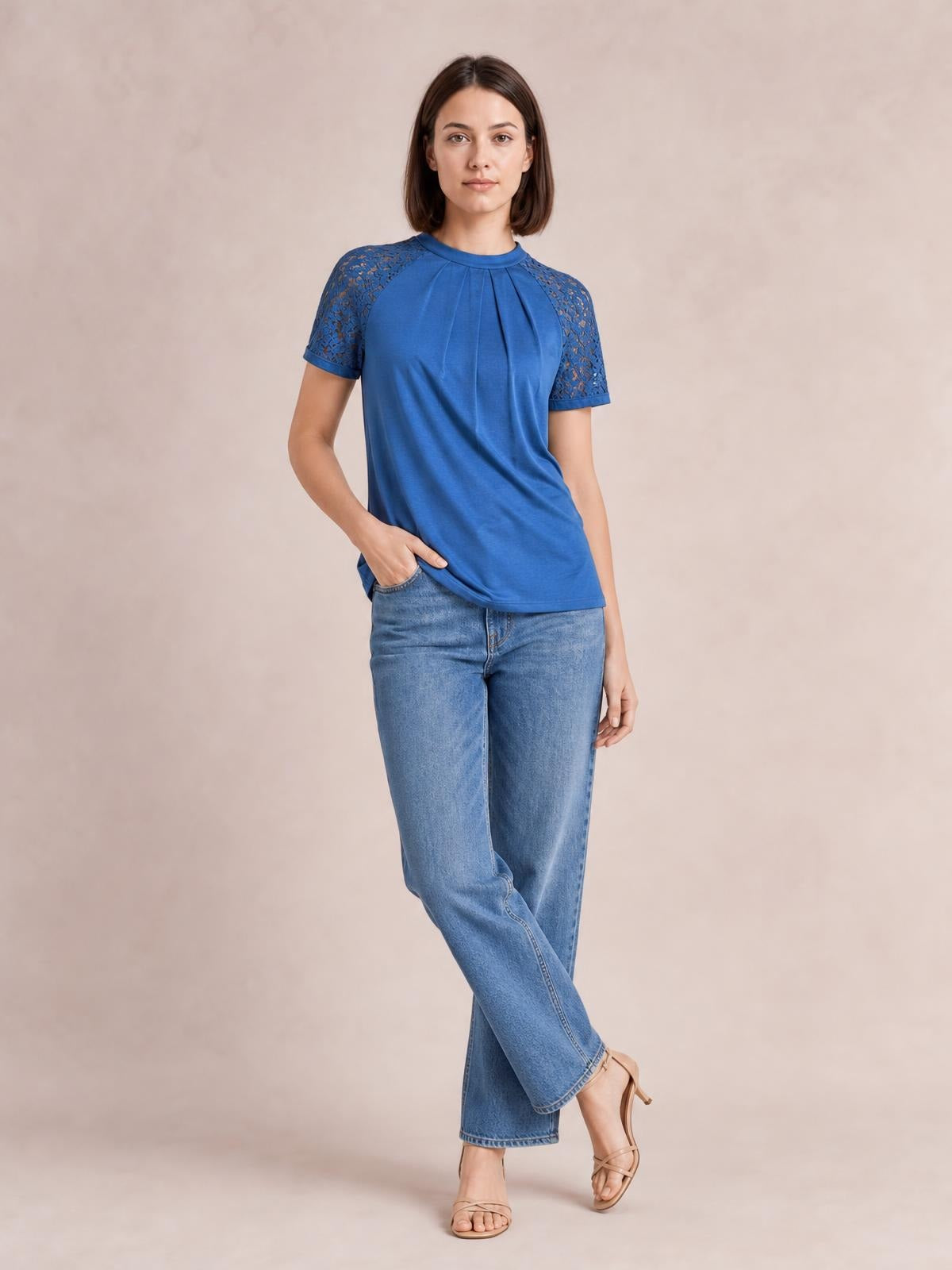 Model poses in a blue round neck short sleeve T-shirt with lace-detailed shoulders and a relaxed silhouette, paired with jeans.