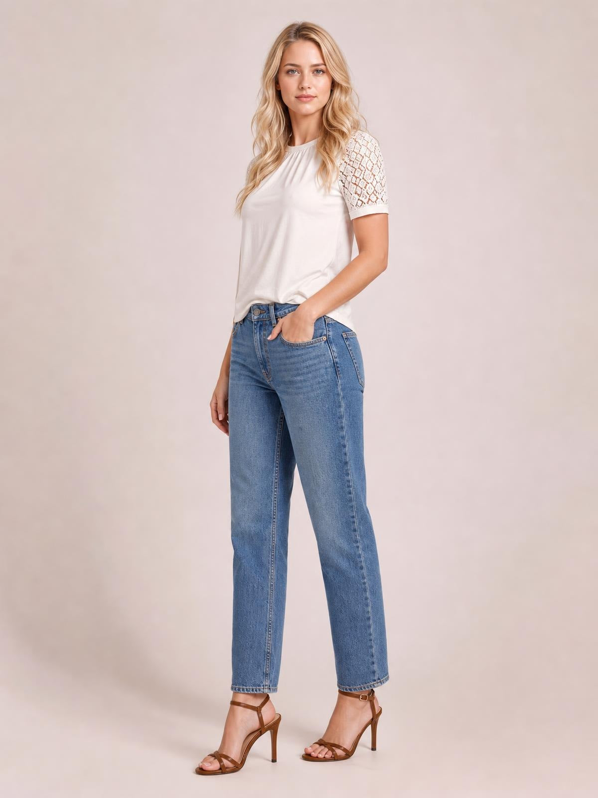 A model poses in a white round neck short sleeve T-shirt with lace-detail sleeves and a relaxed silhouette, one hand tucked into her jeans pocket.