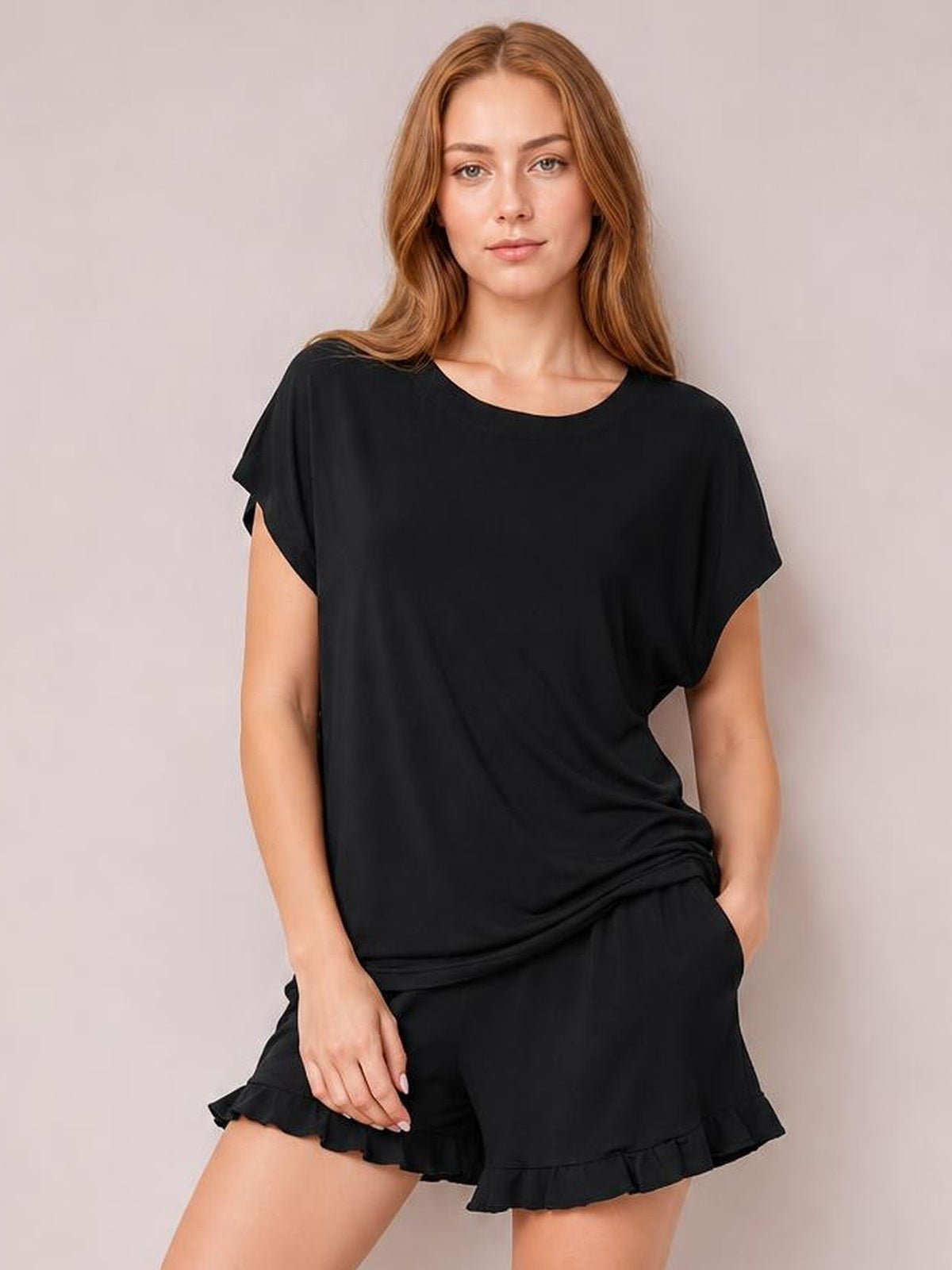 A model poses in a black round-neck short-sleeve T-shirt and drawstring shorts lounge set with a relaxed silhouette and playful frill trim.
