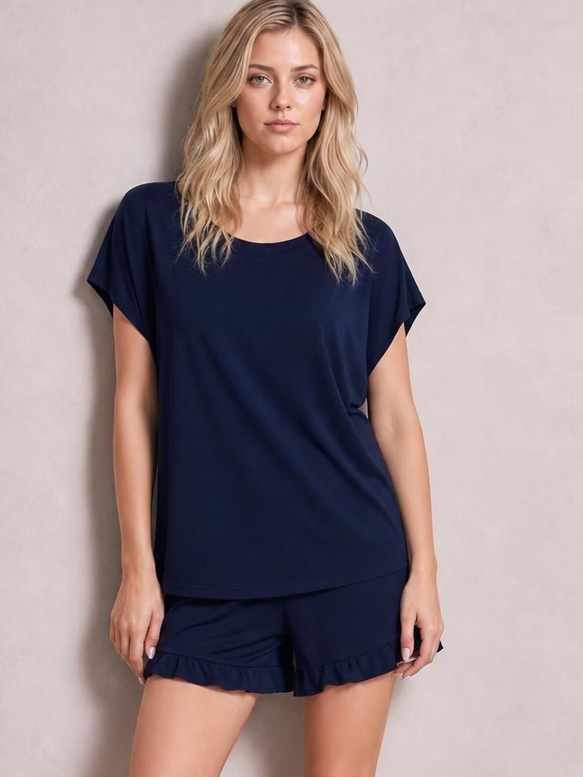 Model stands in a navy lounge set with a relaxed round-neck short-sleeve T-shirt and matching shorts finished with playful frill hems.