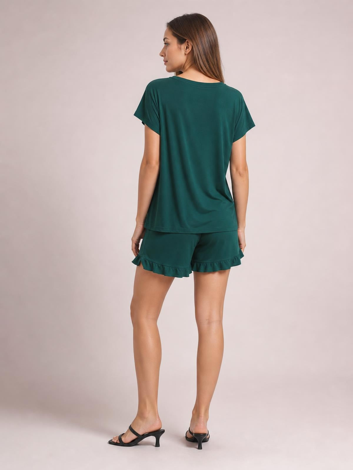 A model looks over her shoulder wearing a deep teal round-neck short-sleeve T-shirt and matching lounge shorts with playful frill hems.
