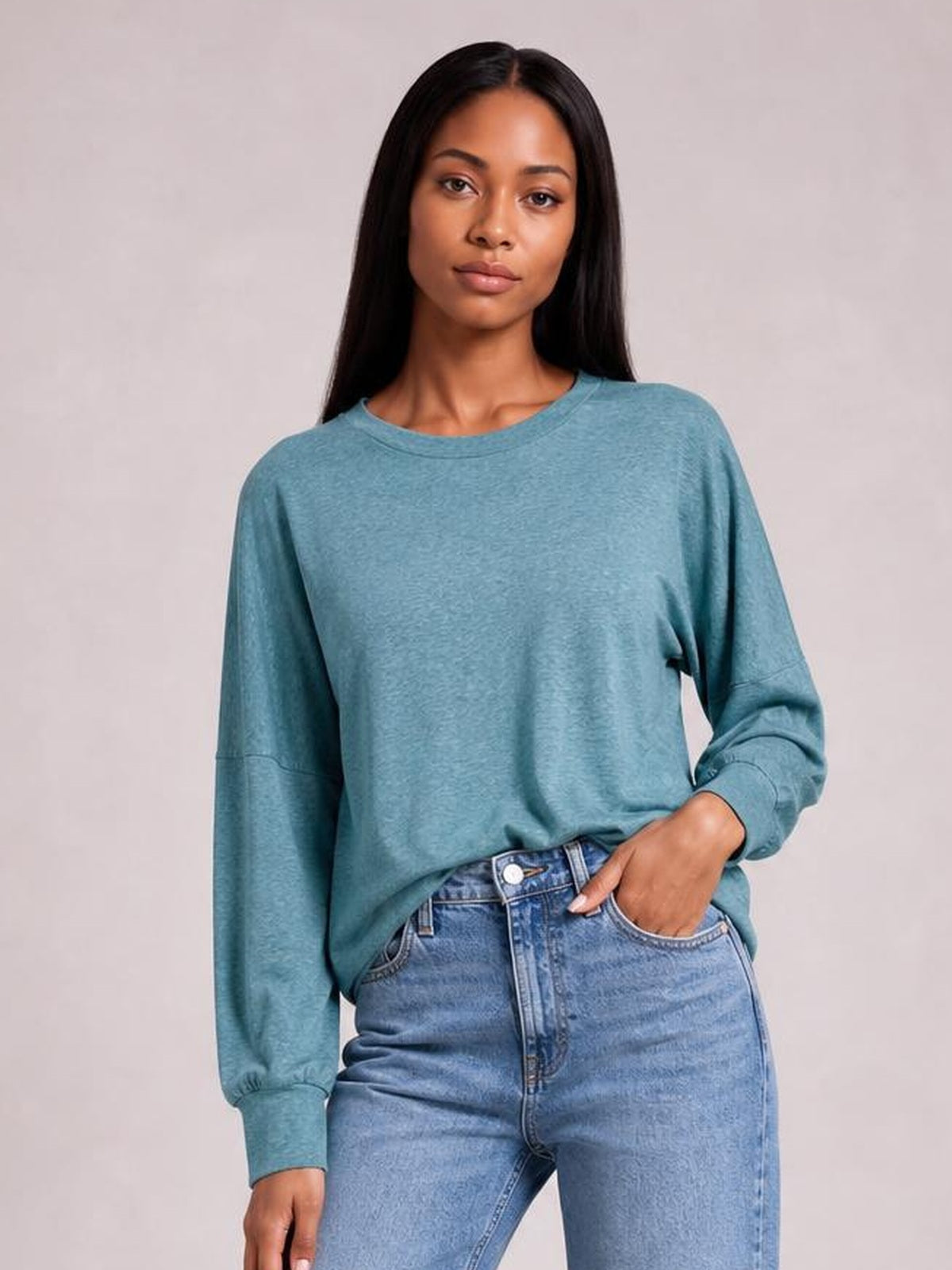 Model wears a teal round-neck T-shirt with a relaxed silhouette, voluminous lantern sleeves, and wide cuffs, posing with one hand in a jeans pocket.