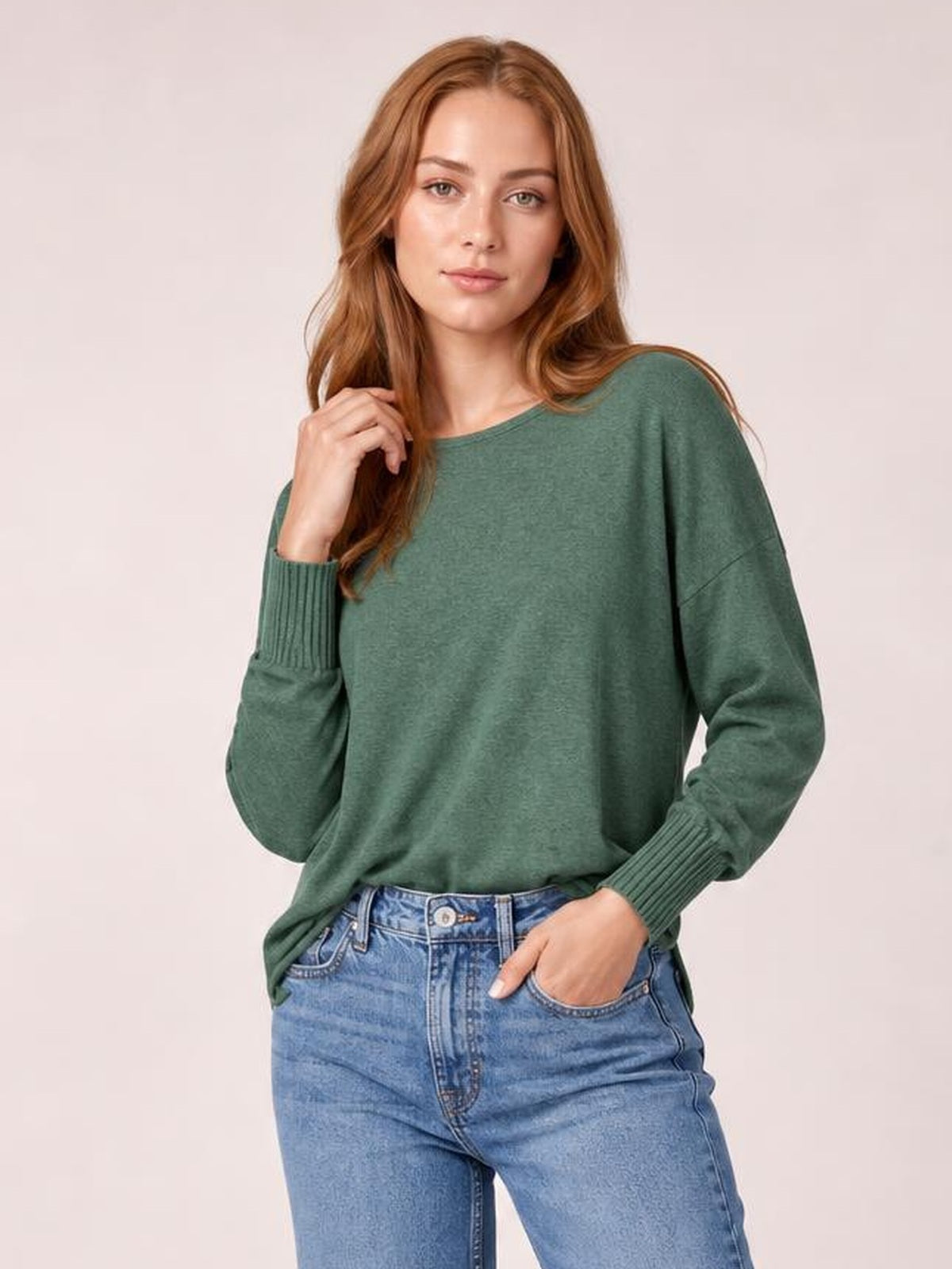 Model wearing a sage green round-neck smocked lantern sleeve T-shirt with a relaxed silhouette and ribbed cuffs, posing with one hand in her jeans pocket.