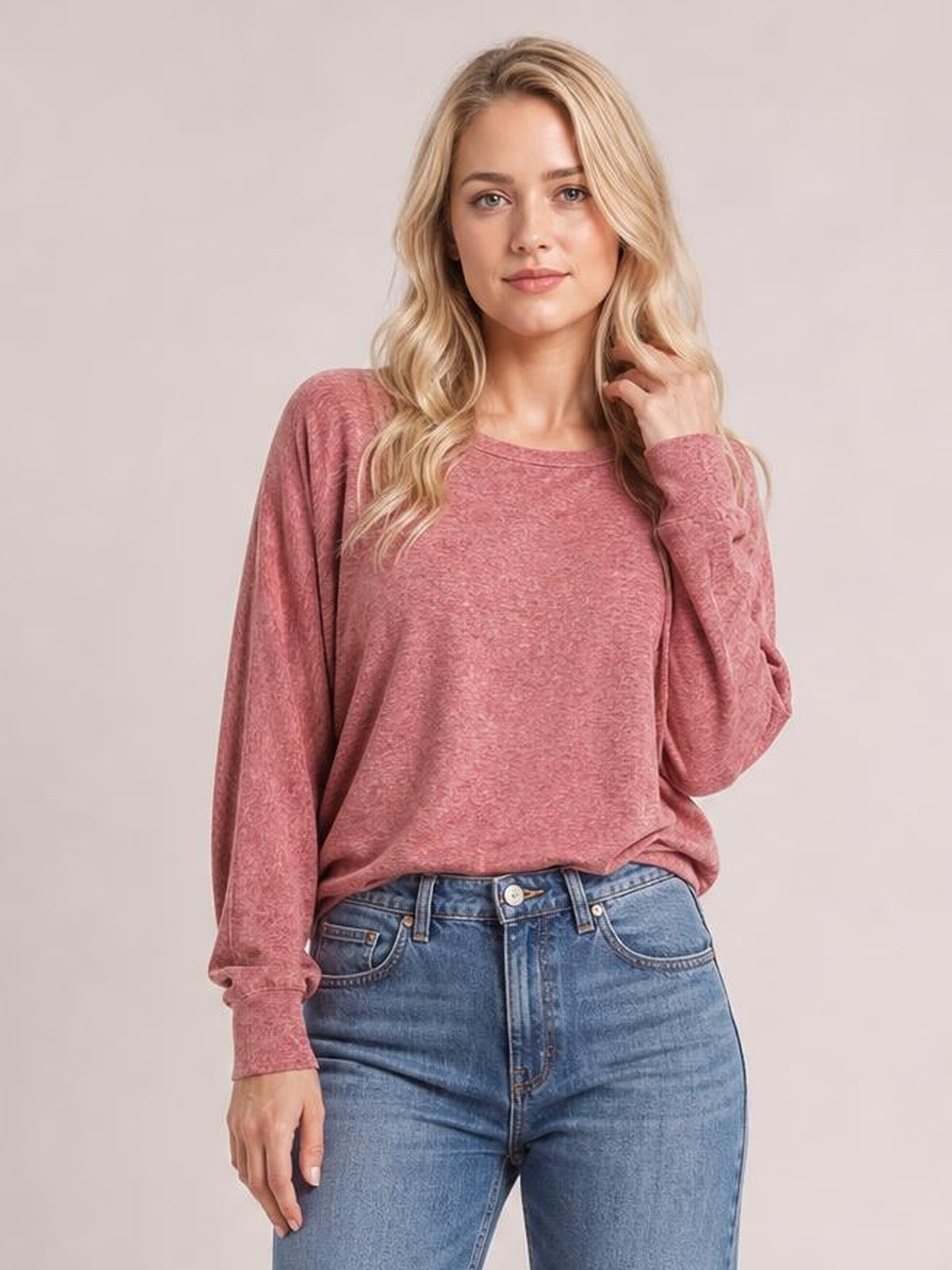 Model wears a dusty rose round-neck T-shirt with long lantern sleeves, smocked cuffs, a relaxed silhouette, and one hand touching her hair.