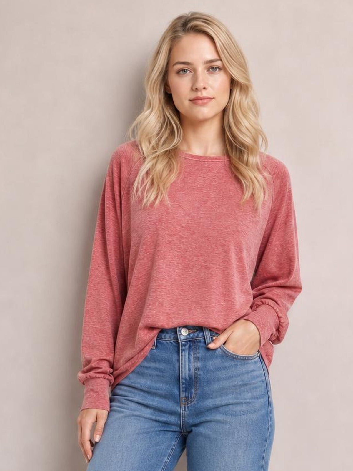 A model wears a dusty rose round-neck smocked T-shirt with relaxed lantern sleeves, gathered cuffs, and a loose silhouette, posing with one hand in her jeans pocket.