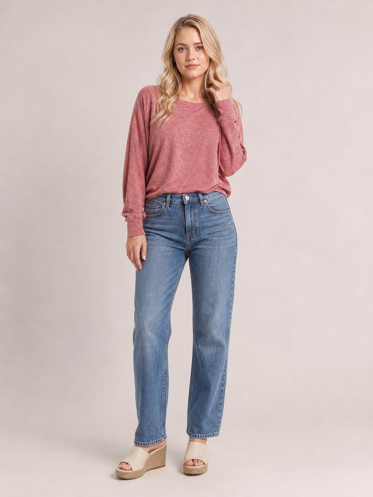 A woman stands in a dusty rose round-neck T-shirt with relaxed lantern sleeves, gathered cuffs, and a softly loose silhouette, touching her hair.