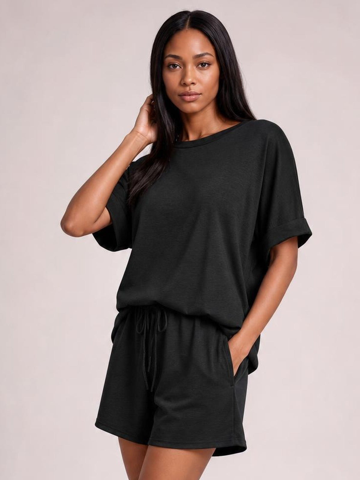Model wears a black round neck T-shirt and drawstring shorts set with a relaxed oversized top, rolled sleeves, and loose knee-length shorts.