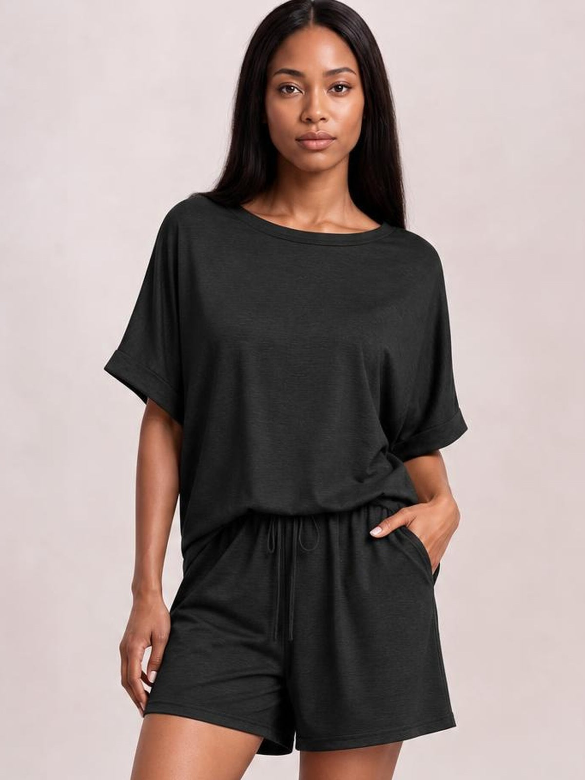 Model poses in a black round neck T-shirt and drawstring shorts set with an oversized top, rolled sleeves, relaxed silhouette, and roomy shorts.