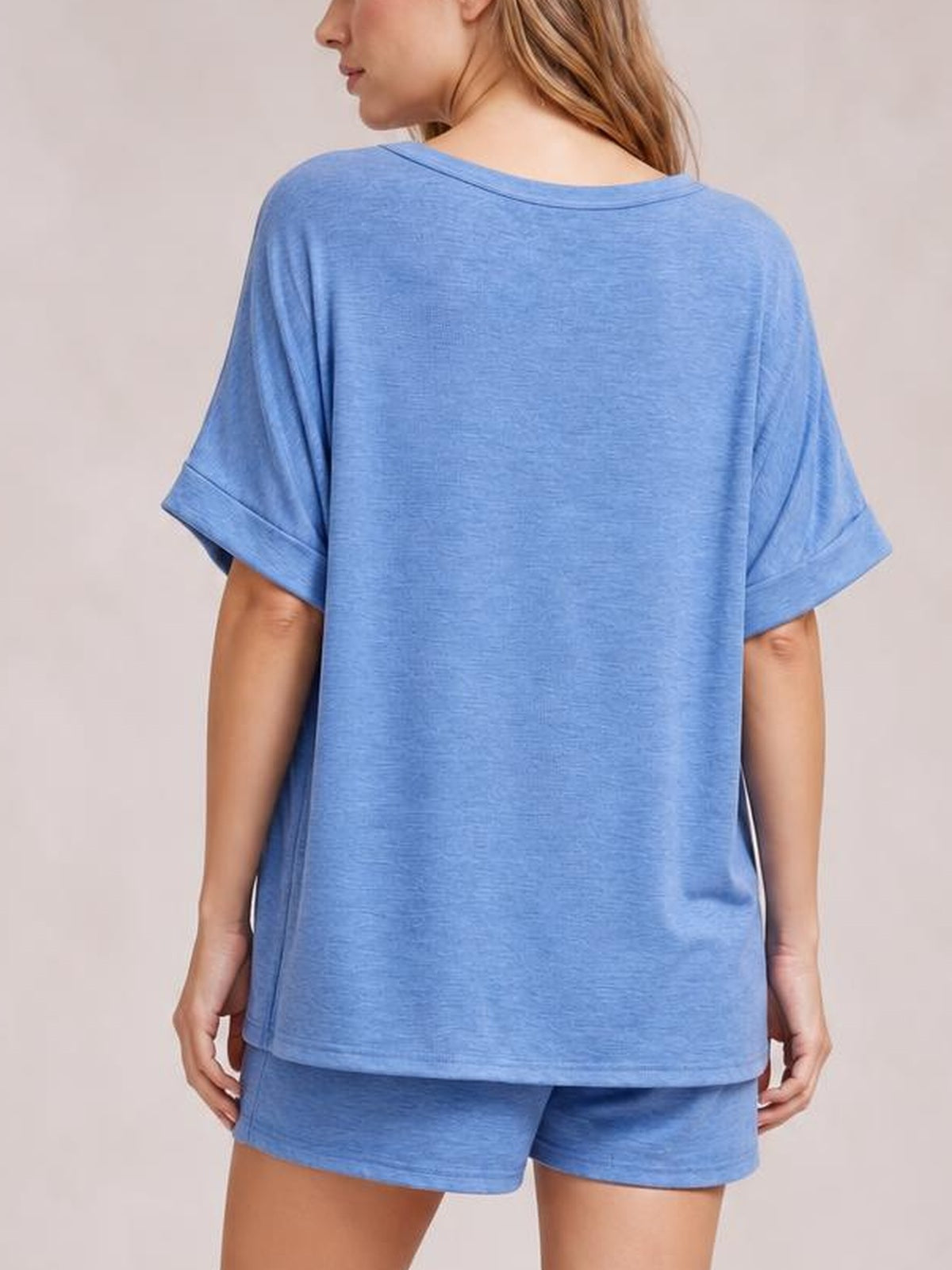 Back view of a woman wearing a blue round neck T-shirt and matching drawstring shorts set with a relaxed oversized silhouette and rolled sleeve cuffs.