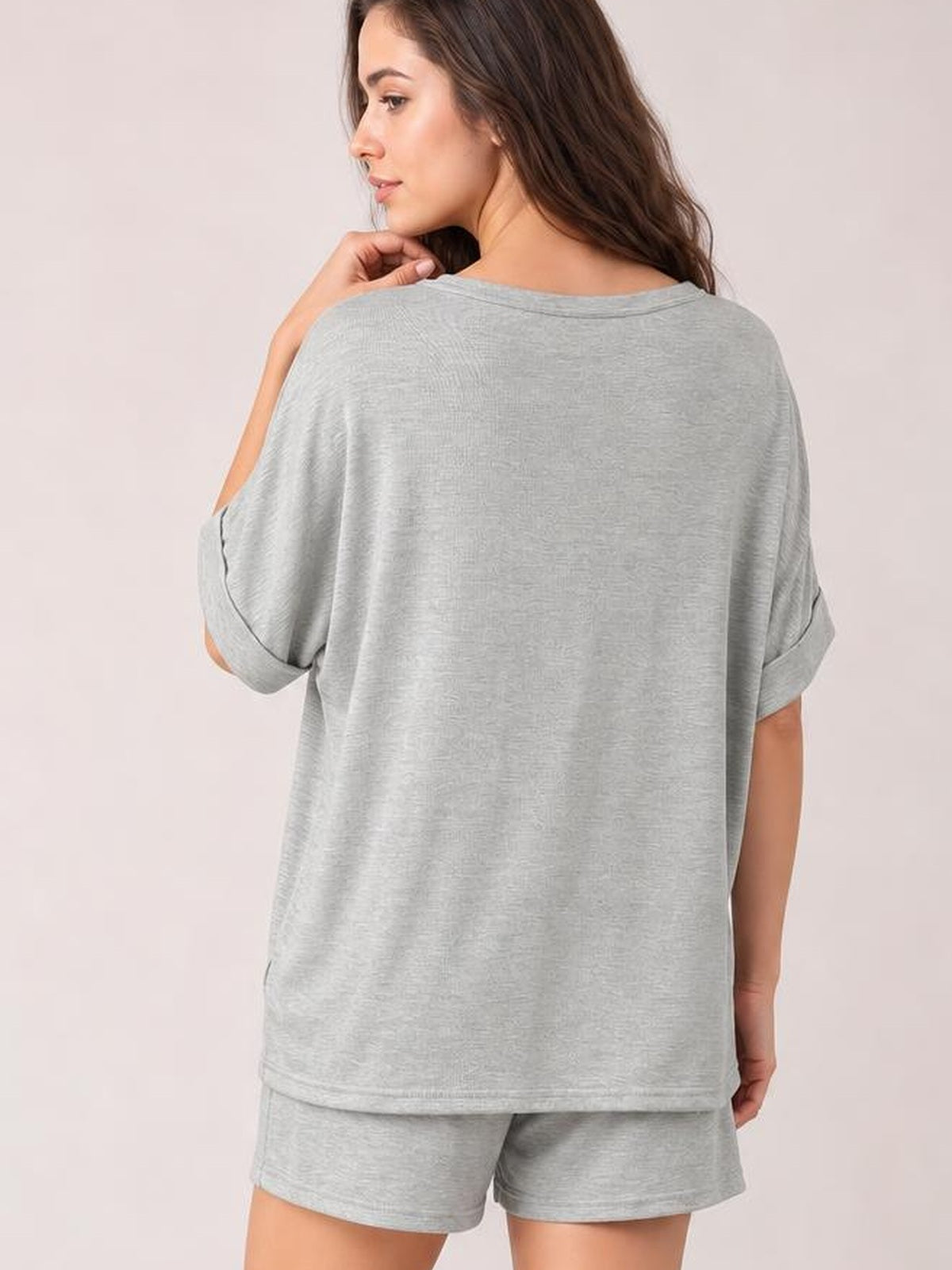 A model looks over her shoulder in a light gray round neck T-shirt and drawstring shorts set with a relaxed oversized silhouette and rolled sleeves.
