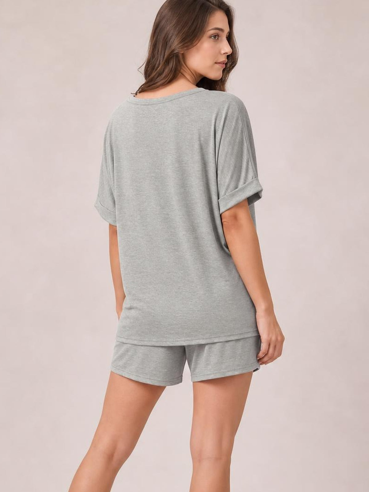 Model poses in a gray round neck T-shirt and drawstring shorts set, showing the relaxed oversized silhouette, rolled sleeves, and casual fit from behind.