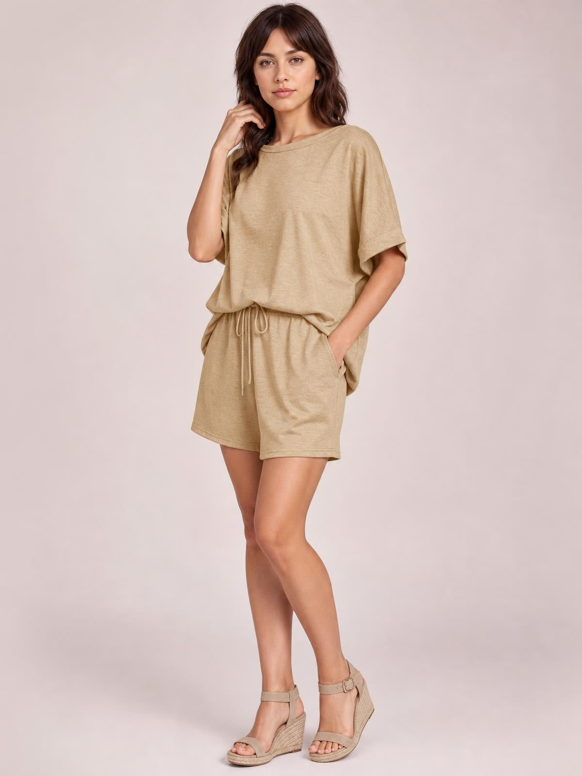 Model poses in a relaxed beige round neck T-shirt and drawstring shorts set with an oversized top, loose silhouette, and side pockets.