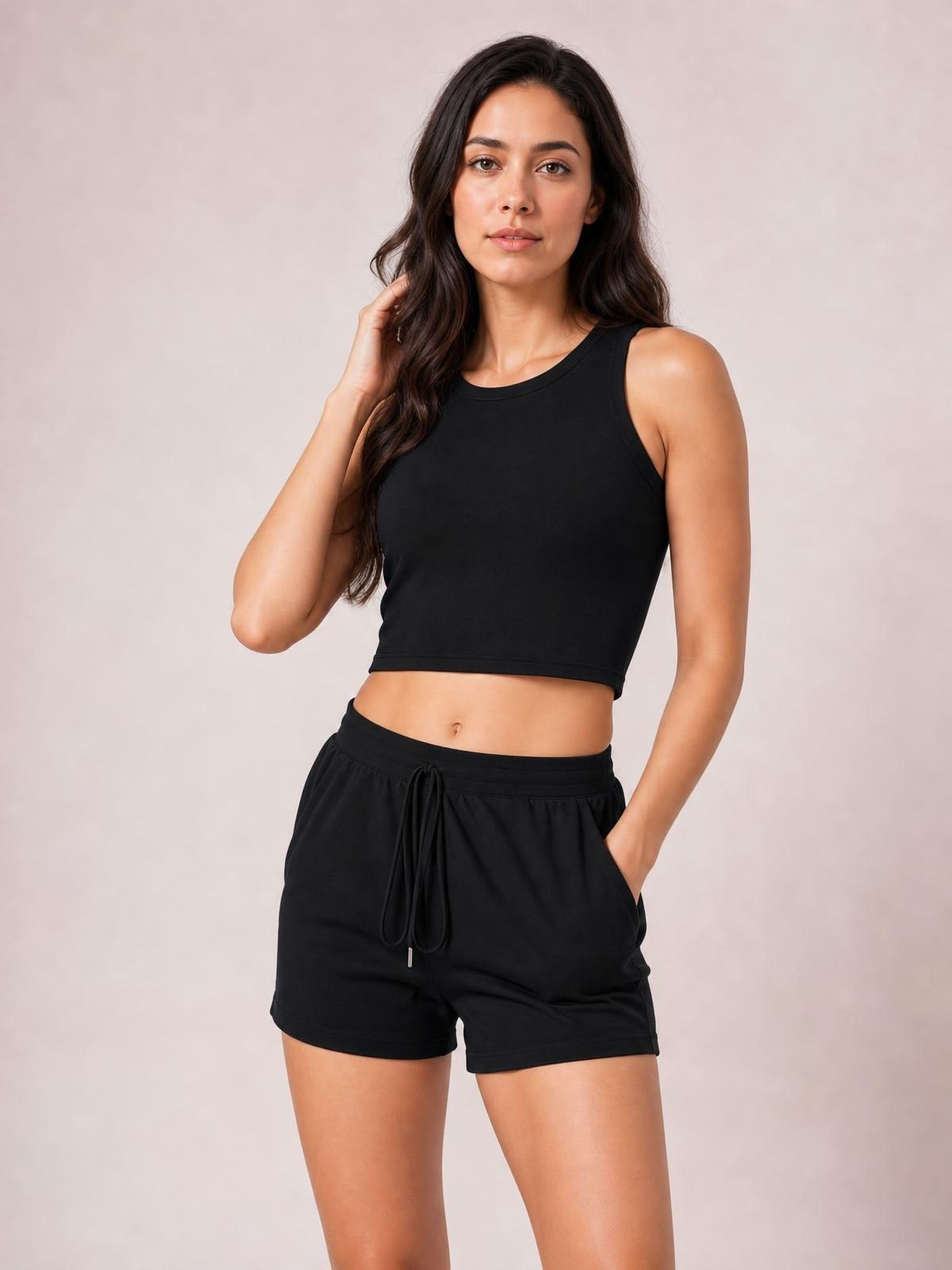 Model poses in a black round neck tank and drawstring shorts set, featuring a fitted cropped silhouette, relaxed shorts, and convenient side pockets.