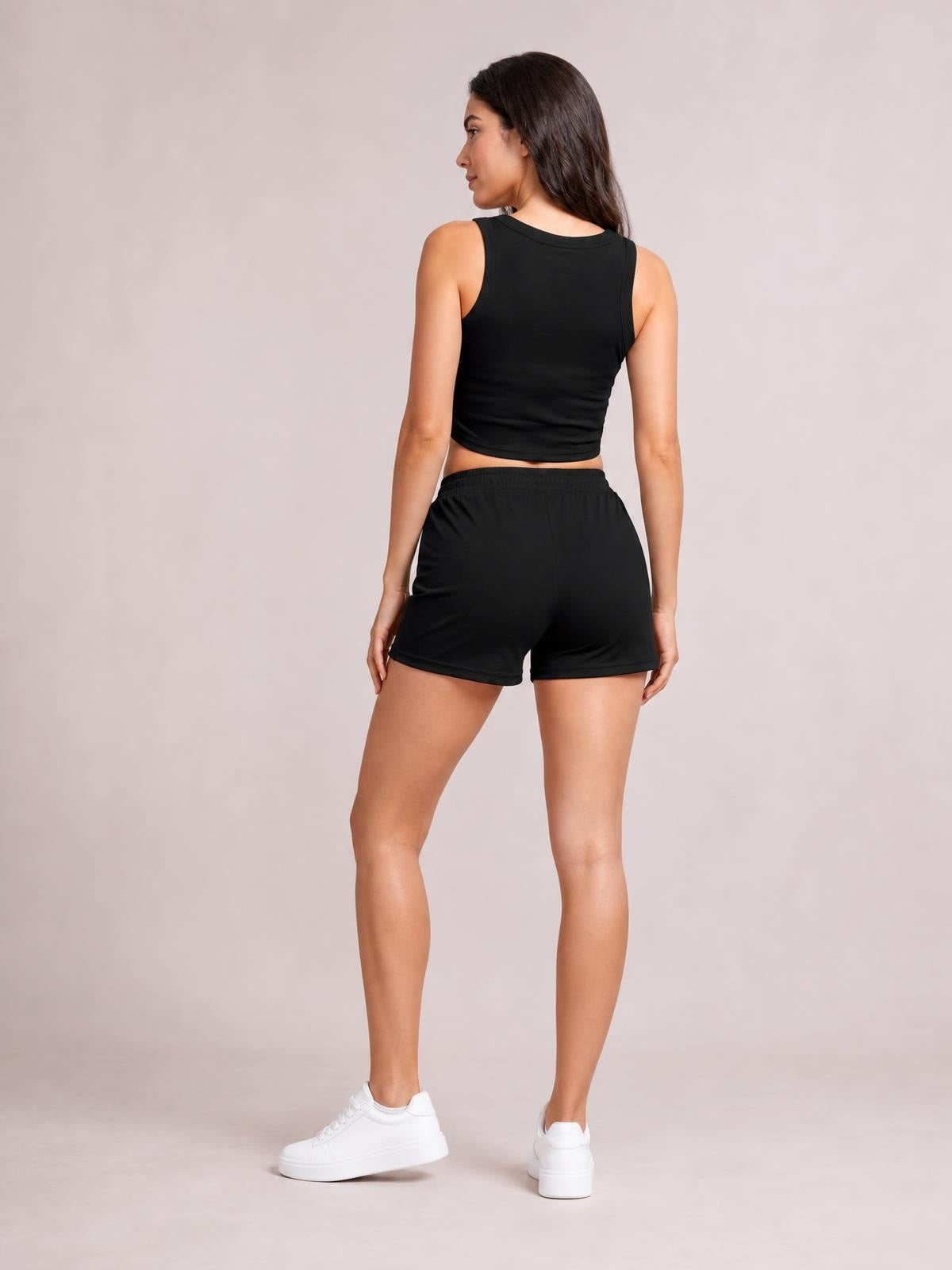 Model shown from behind in a black round neck tank and drawstring shorts set, with a fitted sleeveless top and relaxed short silhouette, looking over her shoulder.