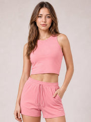 Model poses in a pink round neck tank and drawstring shorts set, featuring a cropped fitted silhouette, relaxed pocketed shorts, and a visible waist tie.