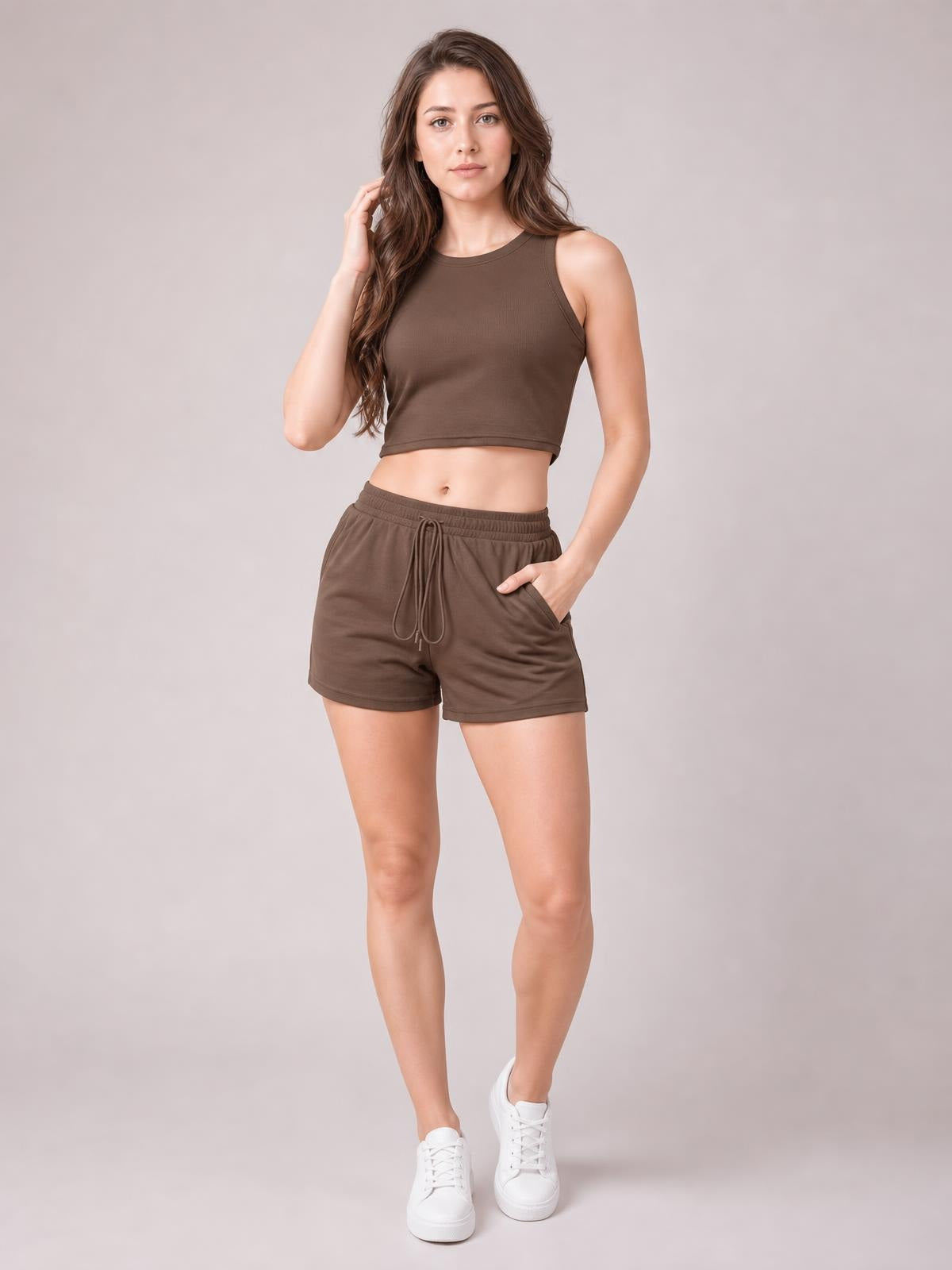 Model poses in a brown round neck tank and drawstring shorts set with a cropped silhouette, elastic waistband, visible pockets, and relaxed shorts.