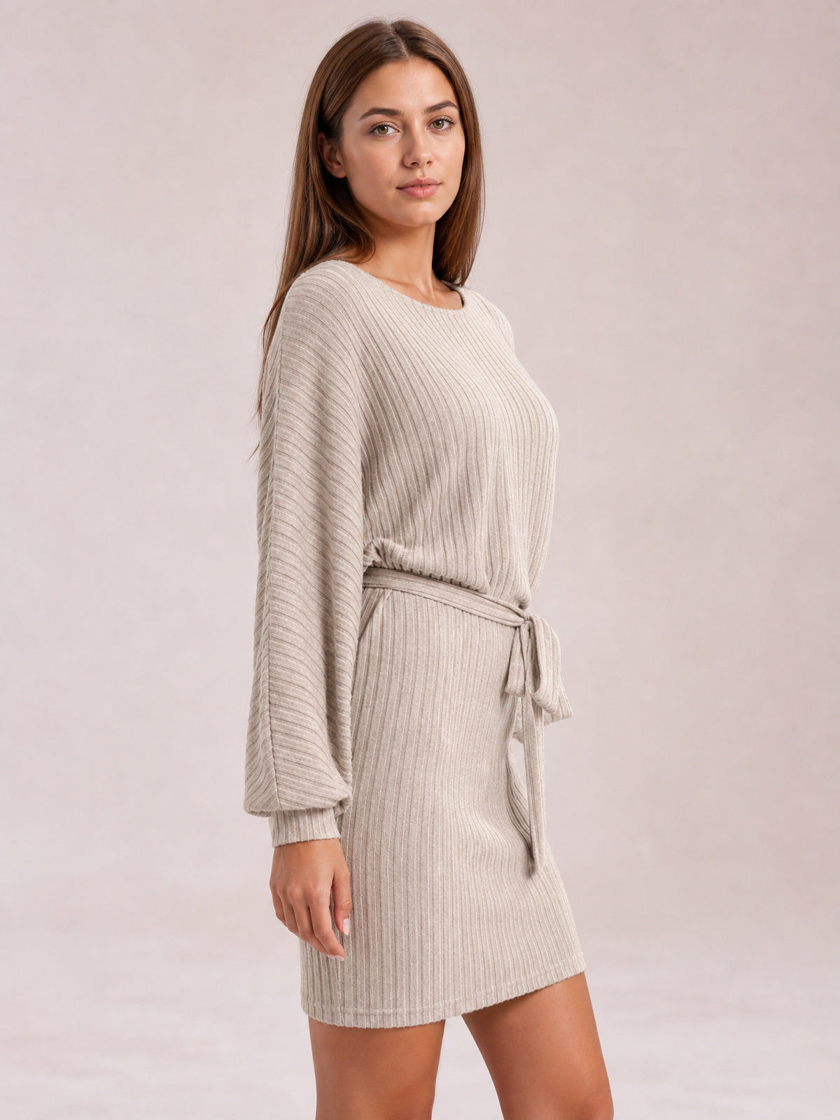 Model poses in a light khaki ribbed mini dress with a round neck, relaxed long sleeves, and a tied waist defining the silhouette.