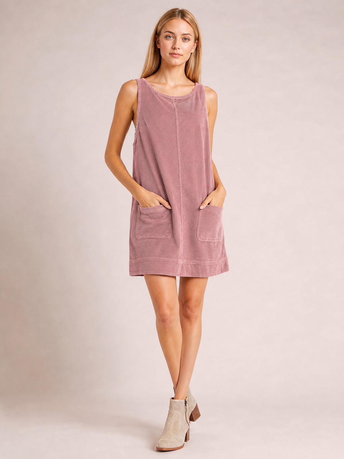 Model poses with hands in the front patch pockets of a dusty rose mini dress featuring a round neck, wide straps, and a relaxed A-line silhouette.
