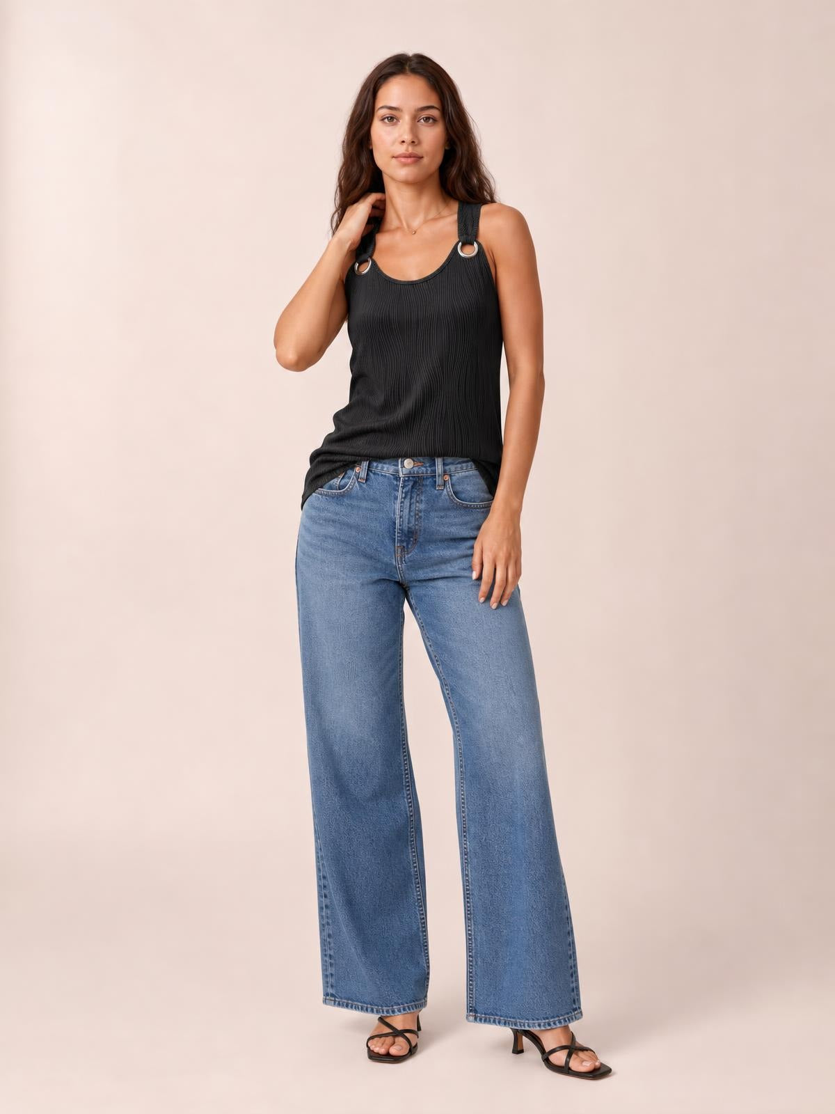 A black round-neck wide-strap tank with subtle vertical texture and ring details is shown on a standing model in a relaxed pose.