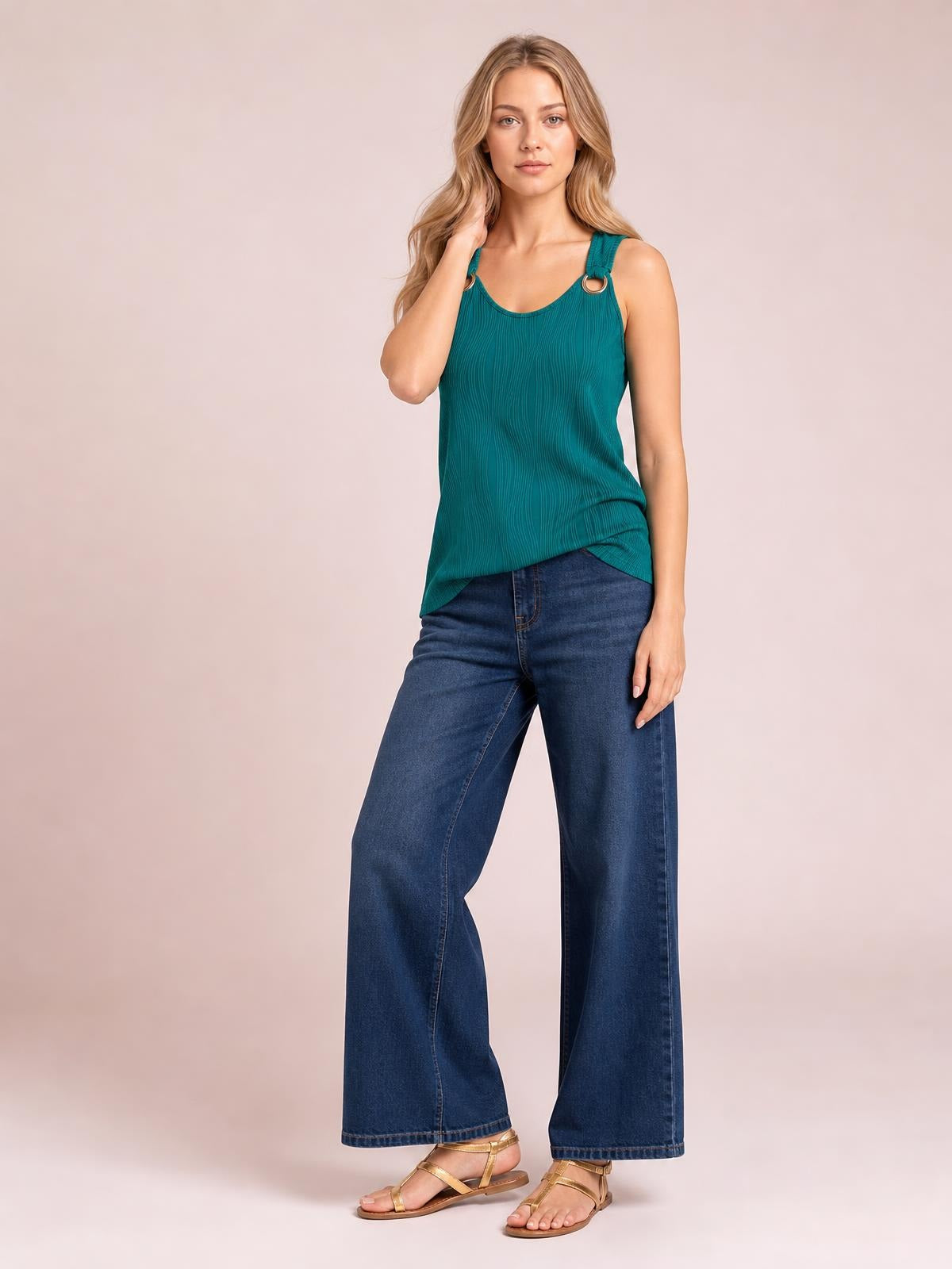 Model poses in a teal round neck wide strap tank with a relaxed straight silhouette, pleated texture, and ring-accented shoulder straps.