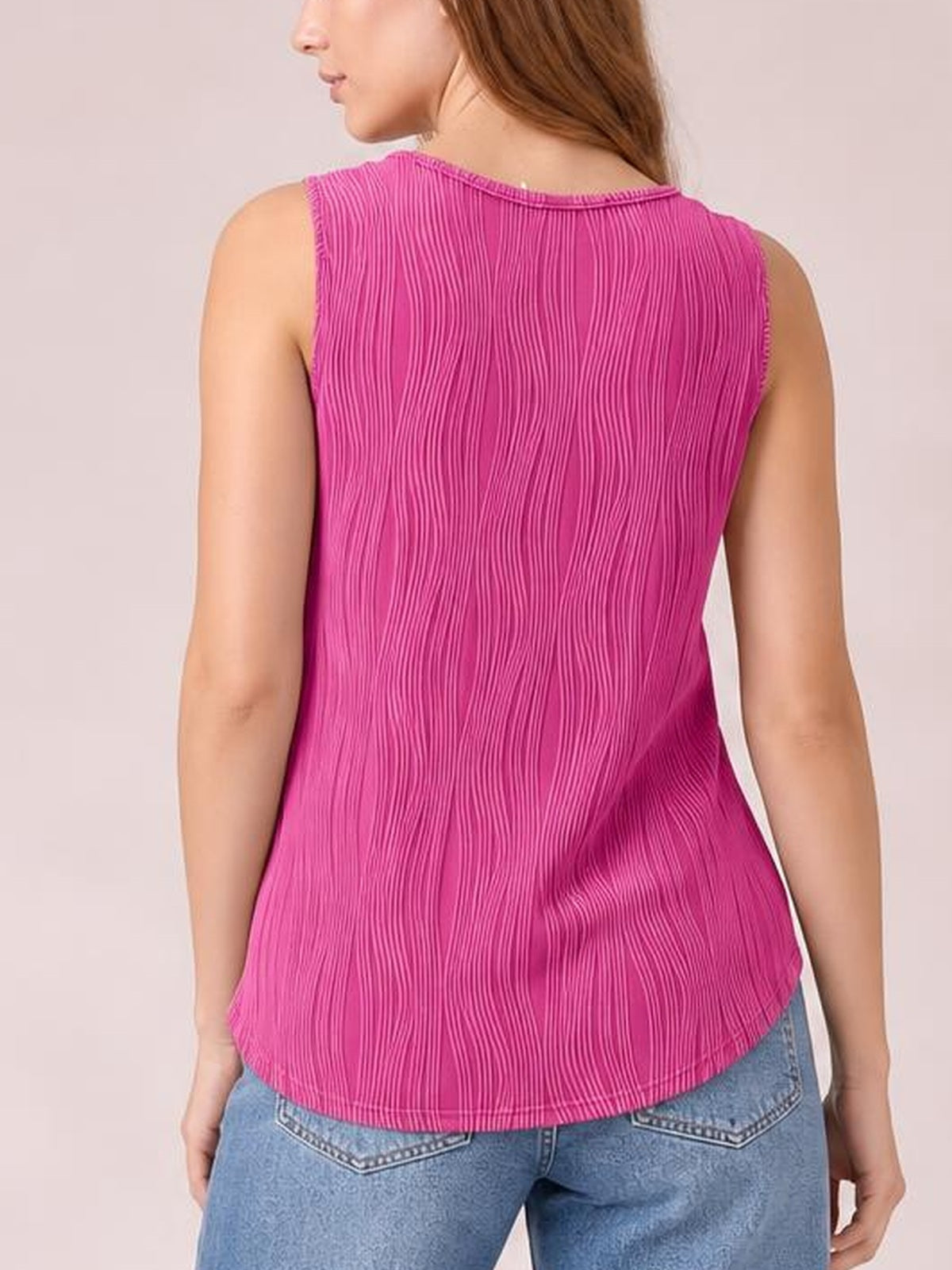 A model stands facing away in a bright pink round neck wide strap tank with vertical textured construction, a relaxed silhouette, and a curved hem.