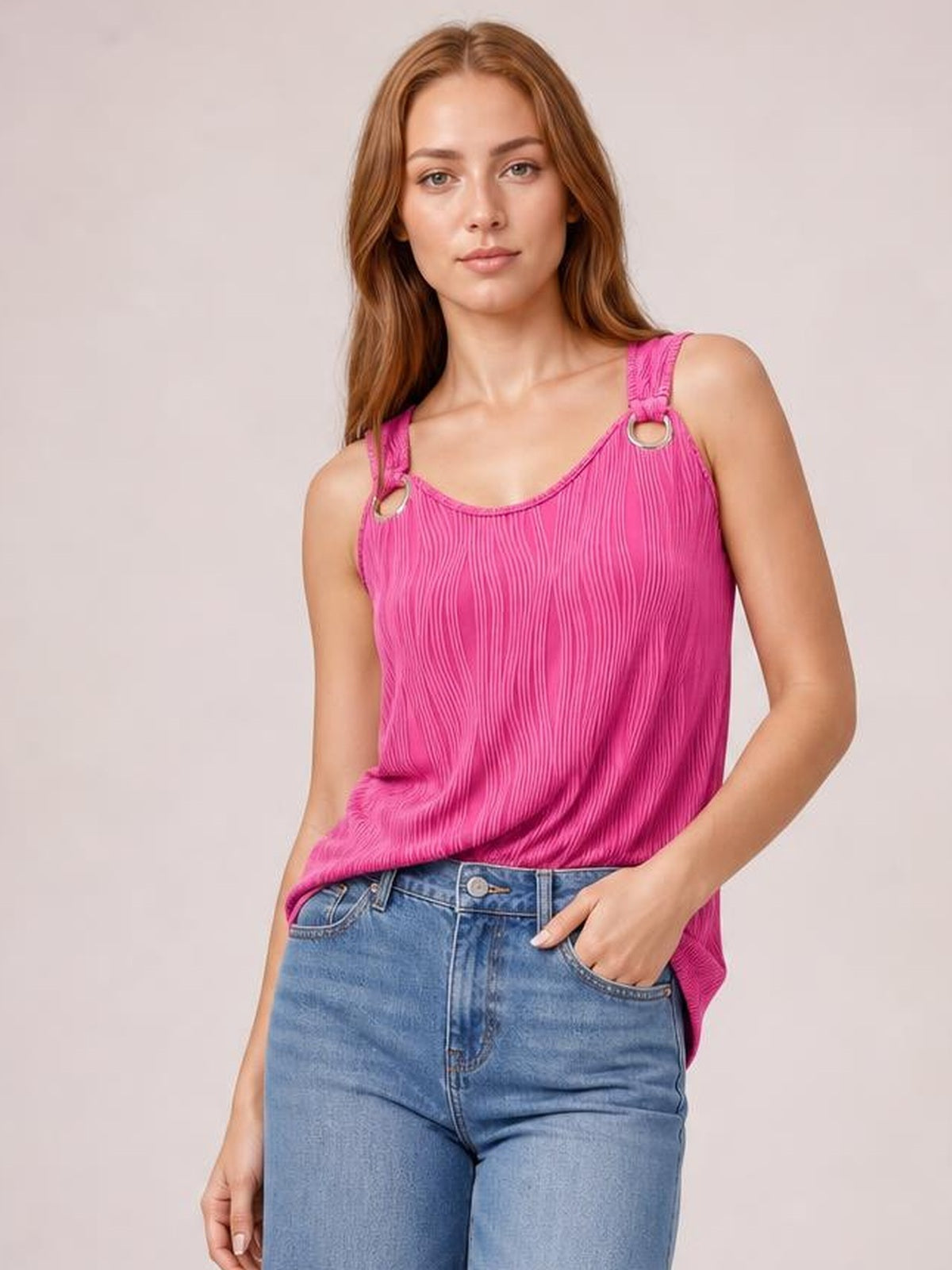 A model wears a pink round-neck wide-strap tank with a relaxed silhouette, vertical textured finish, ring strap accents, and one hand in her jeans pocket.